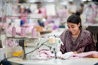 A smiling woman sews at a sewing machine.