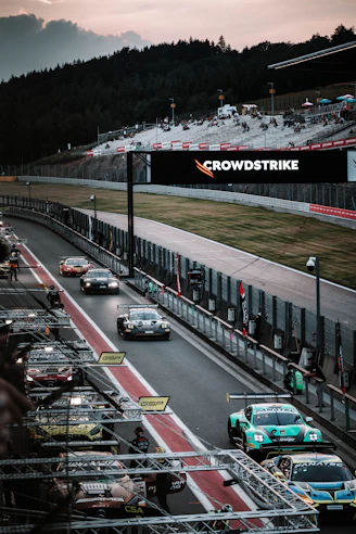 Race cars speed along a track at dusk.