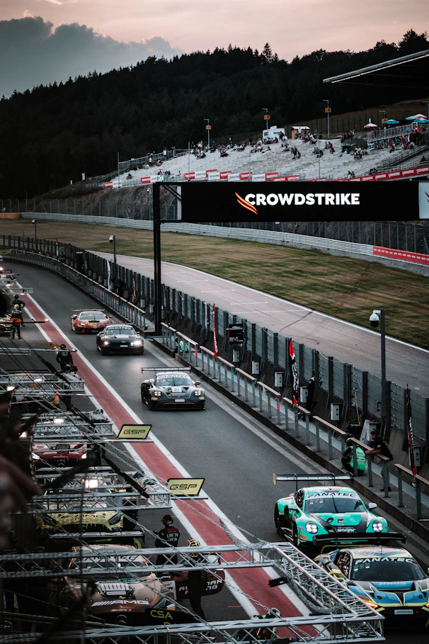 Race cars speed along a track at dusk.