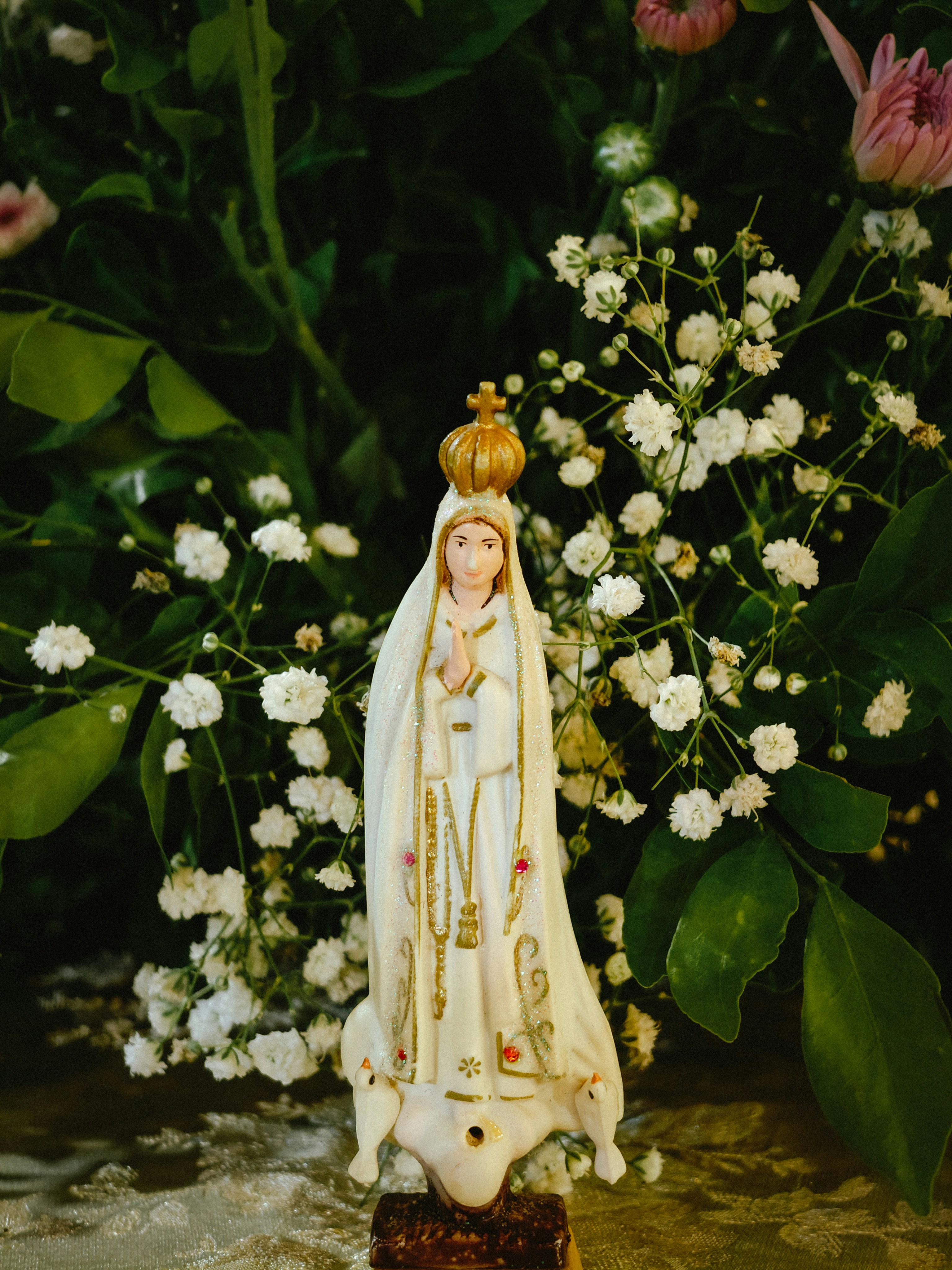 Statue of virgin mary stands among white flowers.