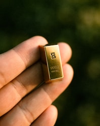 A hand holds a small bar of gold.