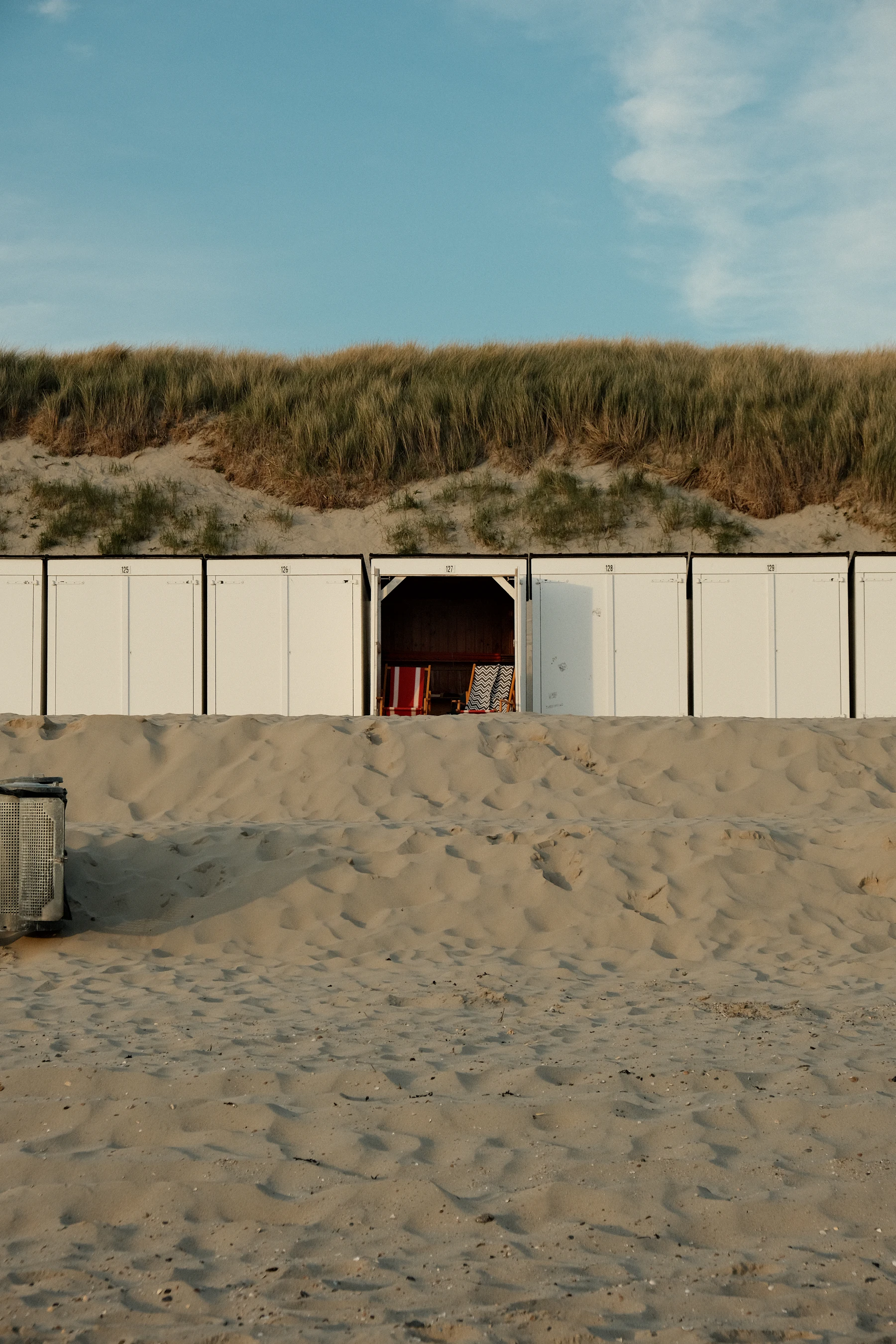 Cabines de plage blanches alignées au pied d'une dune