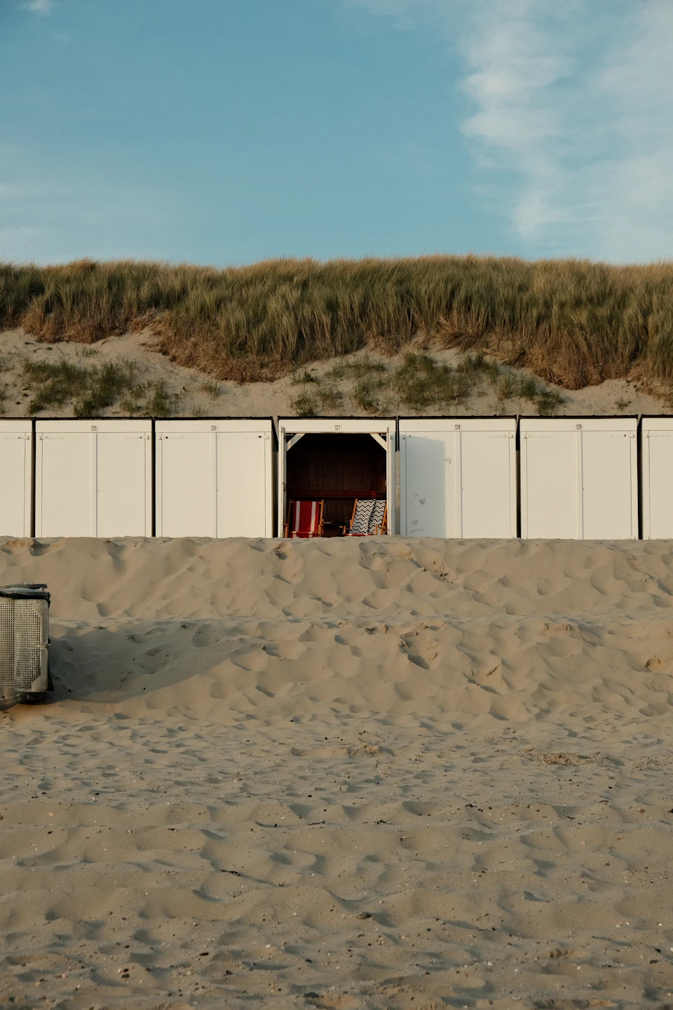Witte strandcabines op een rij aan de voet van een duin