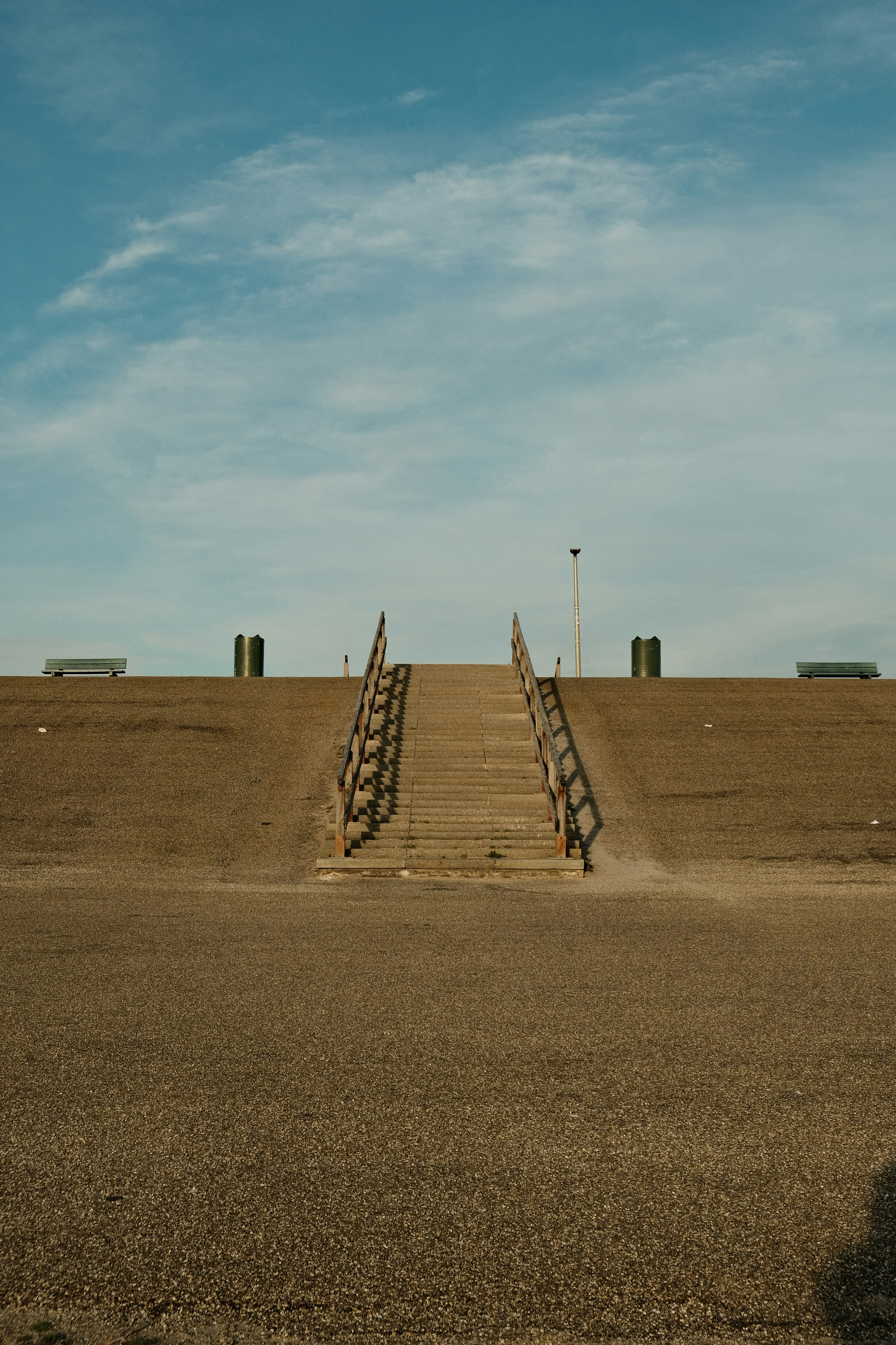 Stairs lead upward to a grassy hill under a blue sky.