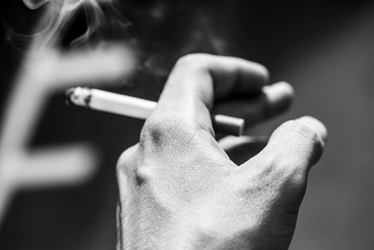 Hand mit einer brennenden Zigarette als Symbol für gelegentliches Rauchen