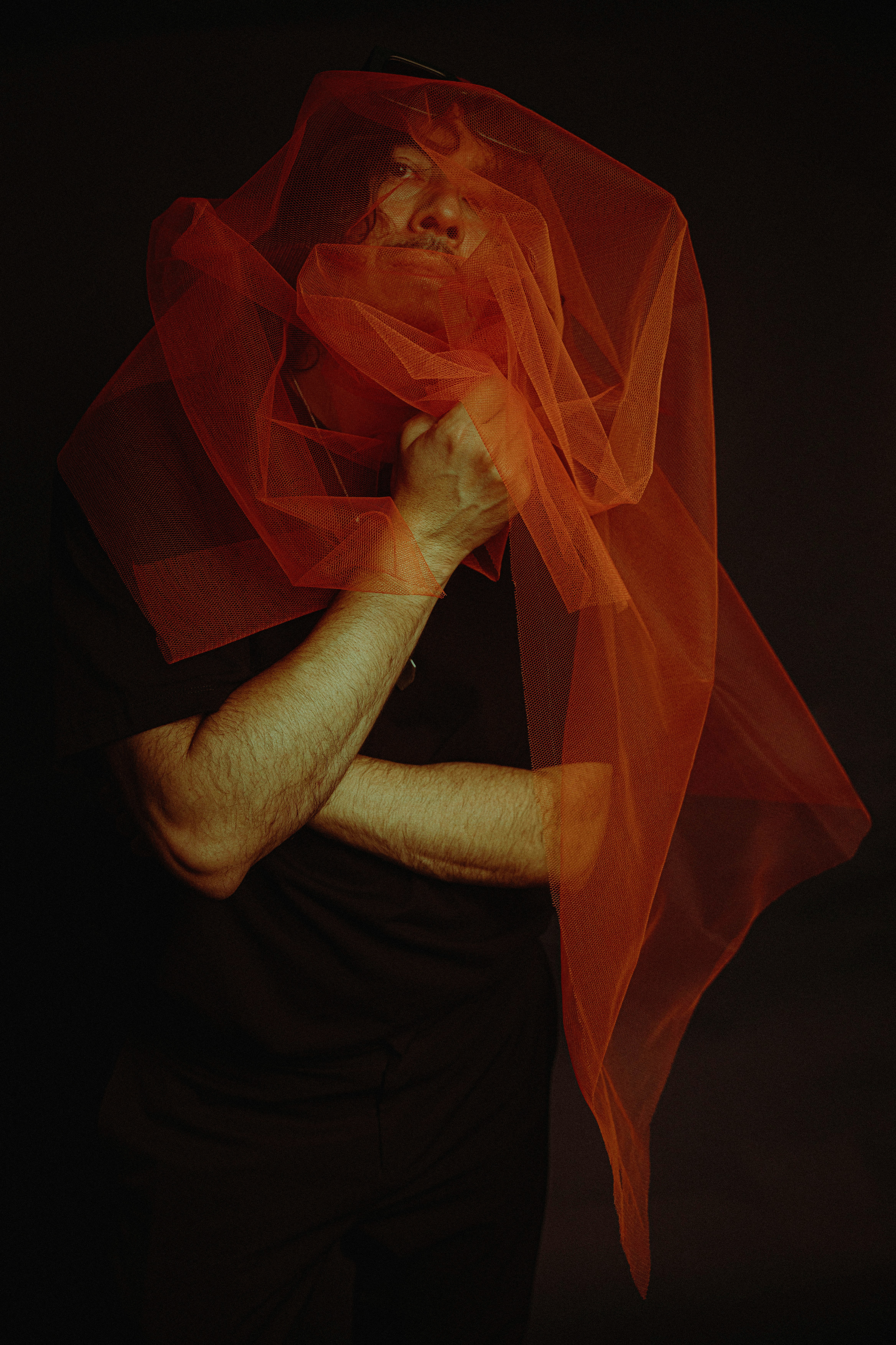 Man obscured by orange fabric against a dark background.