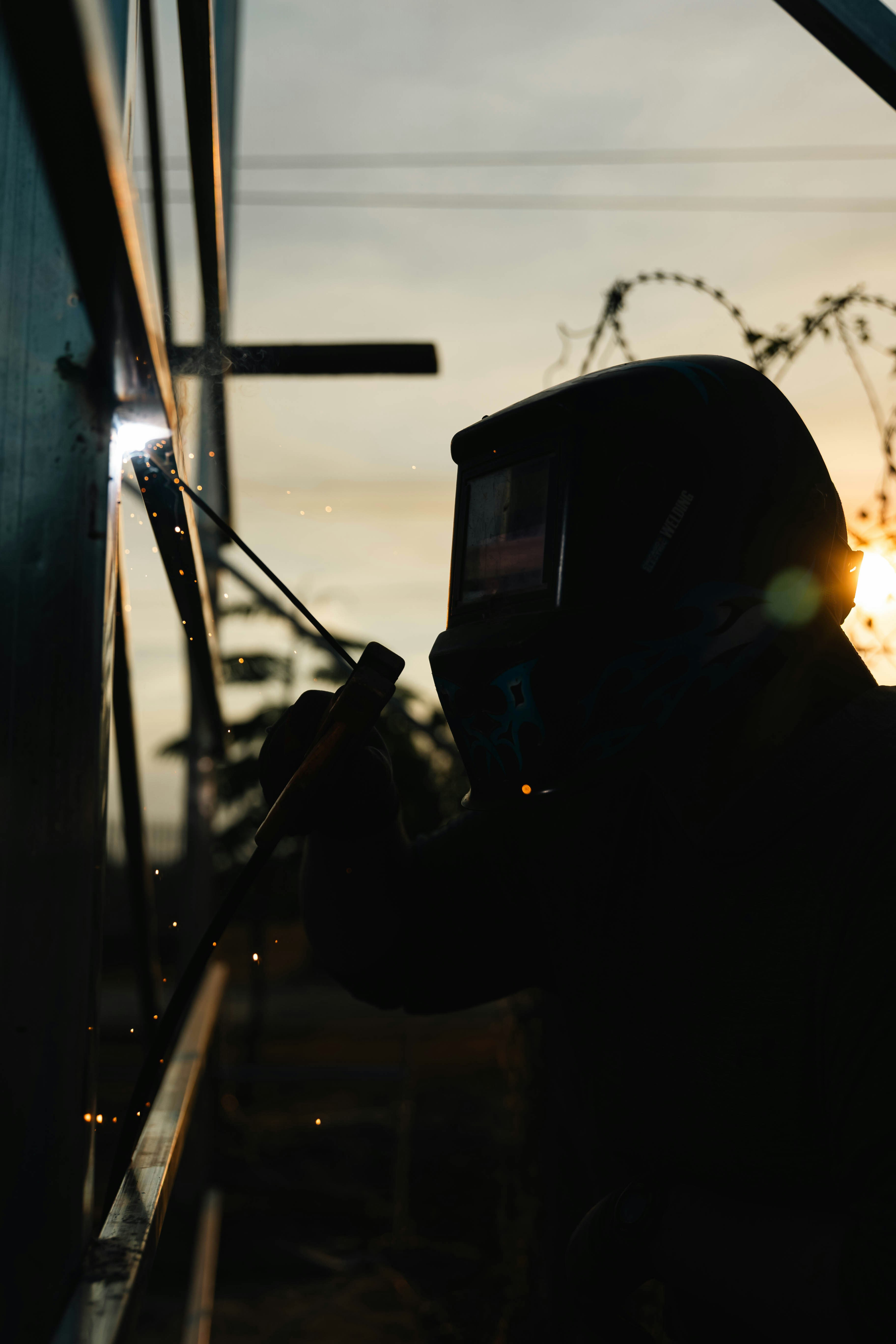 Welder silhouetted against golden sky creating sparks.
