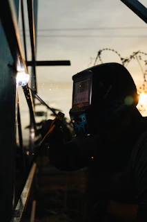 A welder works, sparks fly against the sunset.