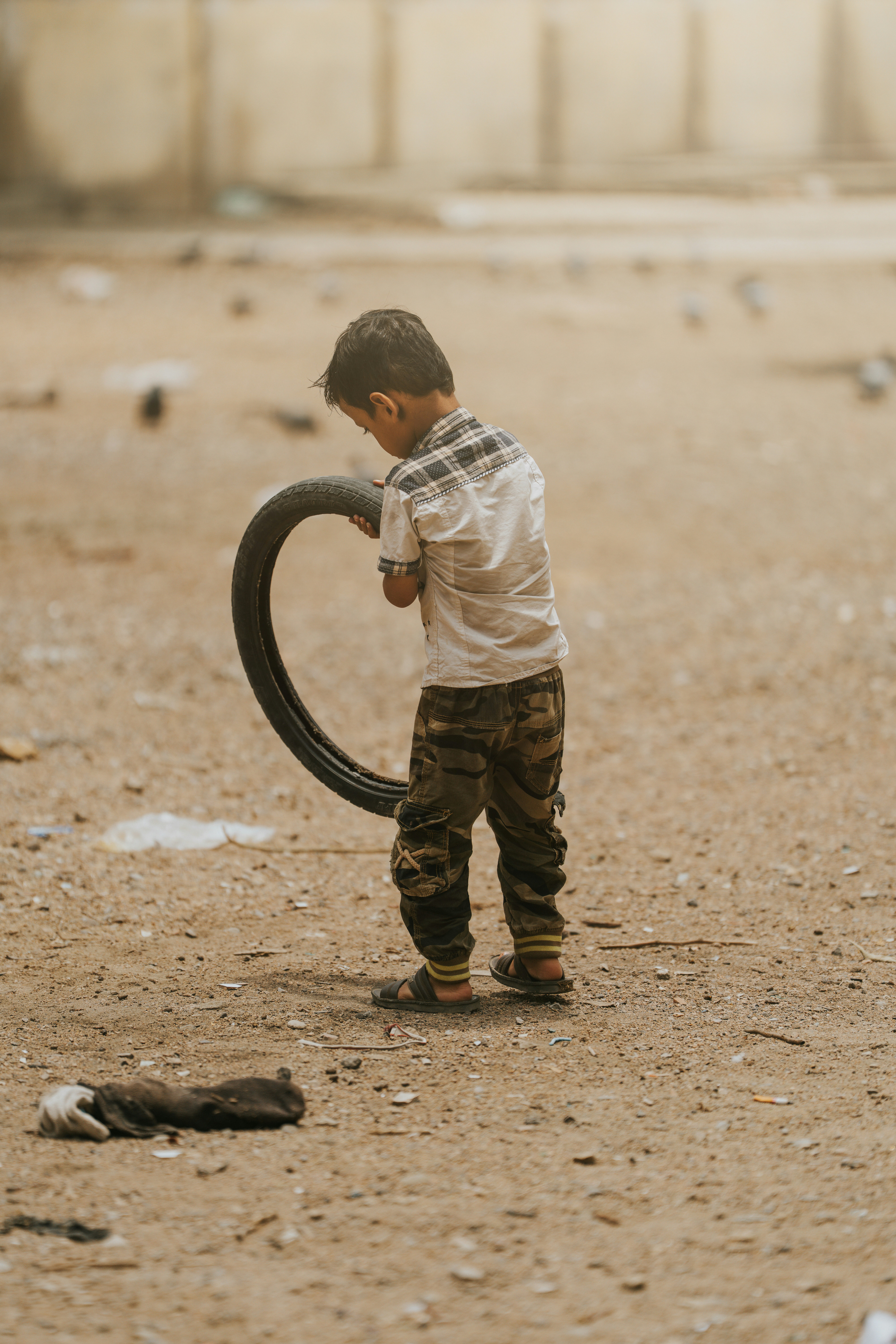 A boy plays with a tire in a dusty field.