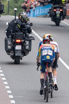 Cyclists race behind a motorcycle on a course.