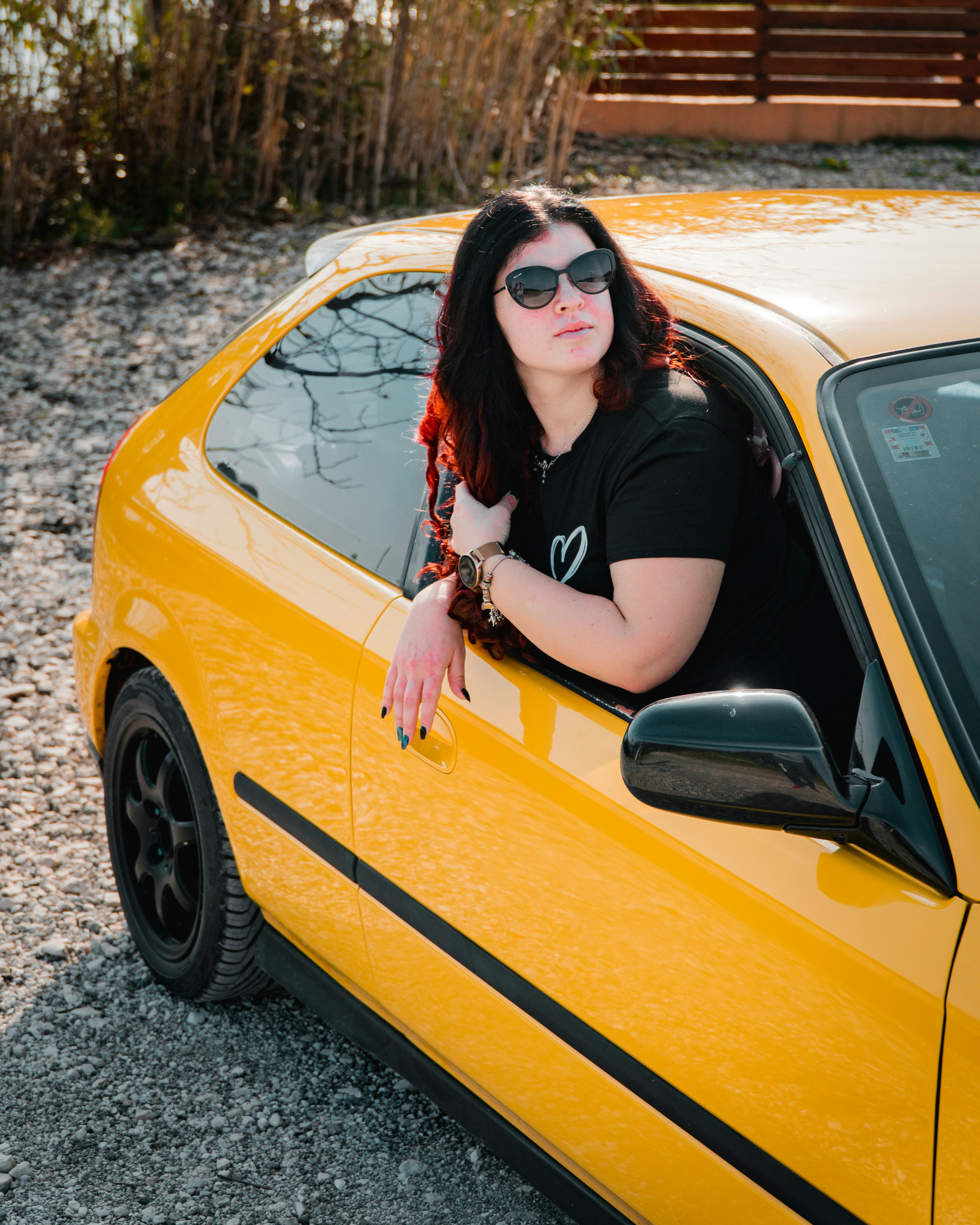 A woman poses in a yellow car.