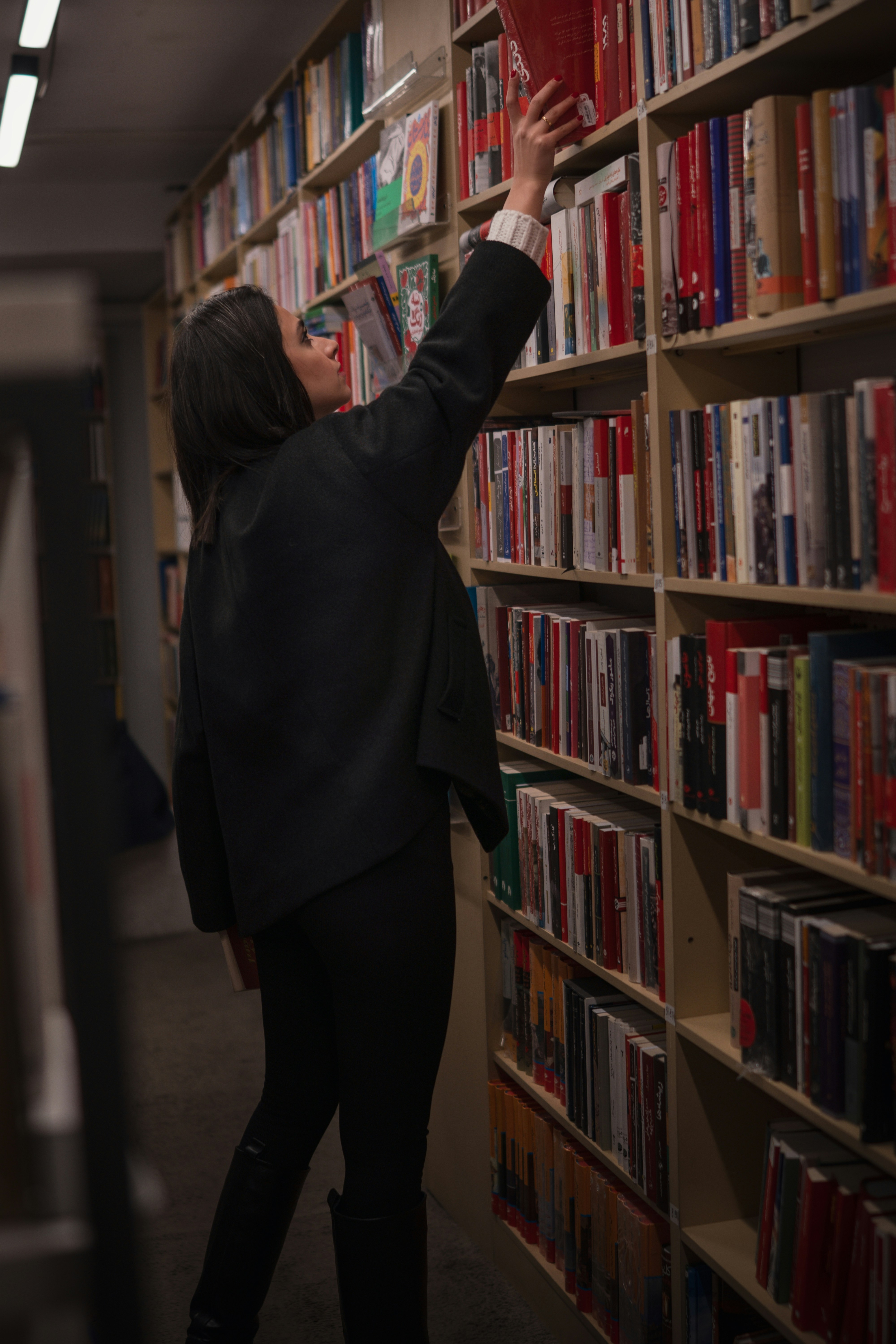 Woman reaches for a book on a library shelf.