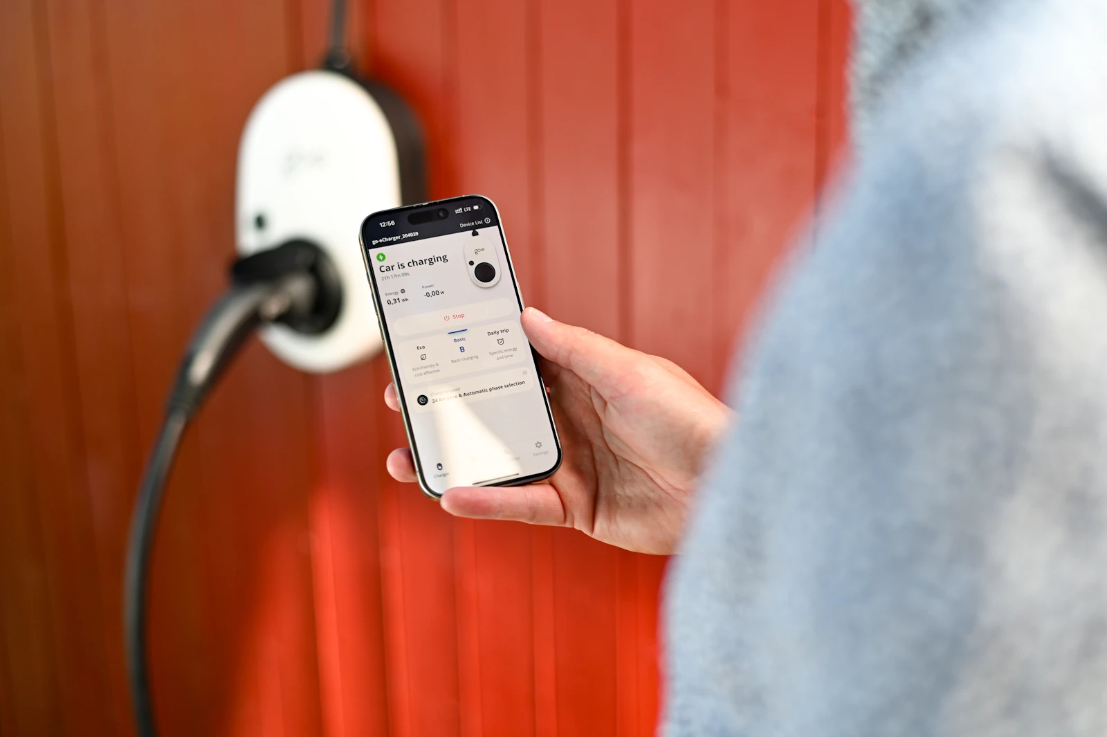 Una persona sigue en la app del móvil la carga desde un wallbox de pared con el cable conectado