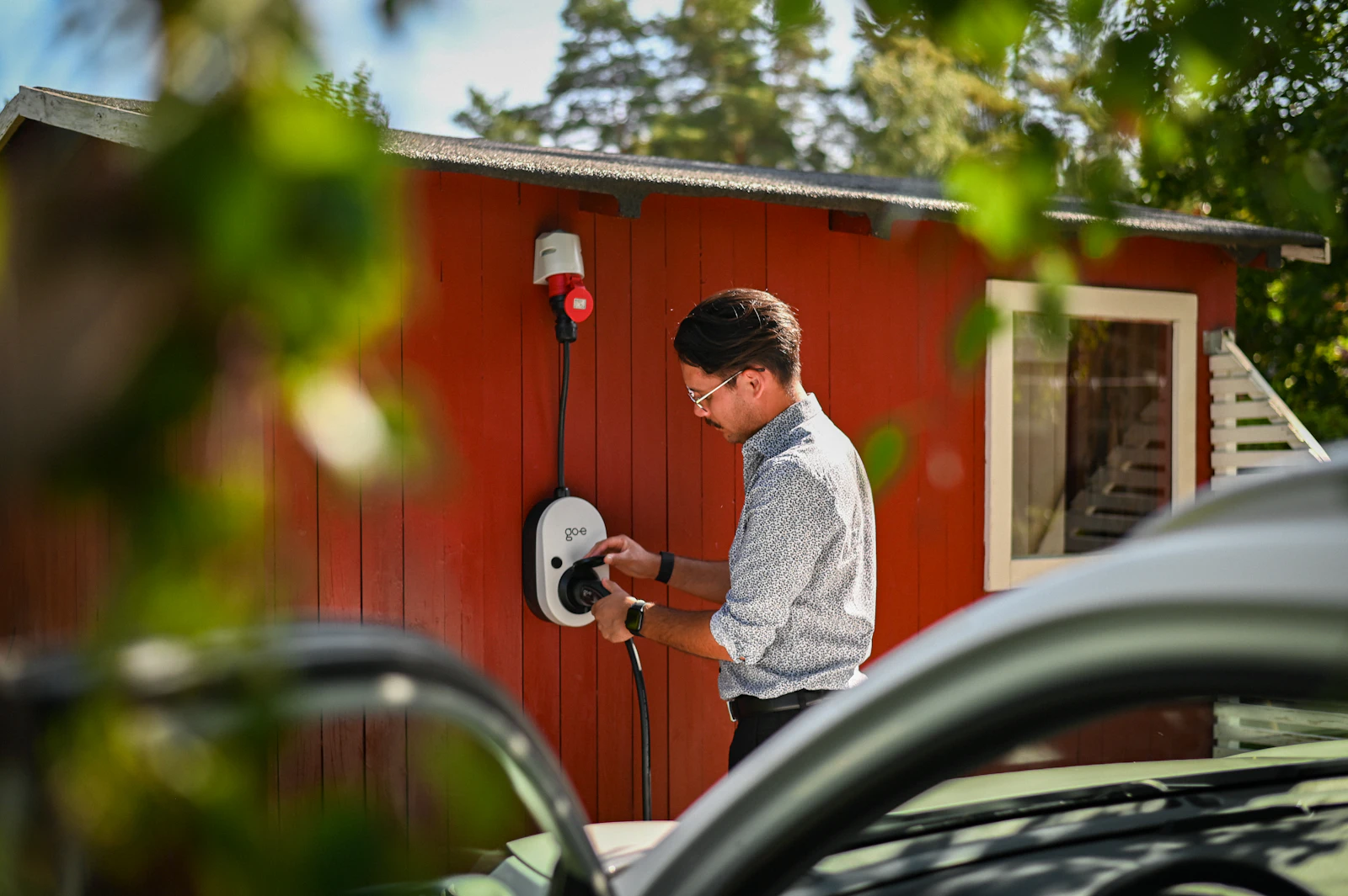 Un particulier branche sa voiture électrique sur sa borne de recharge à domicile