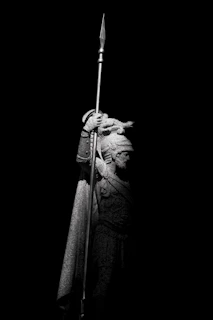 A statue of a warrior stands holding a spear.