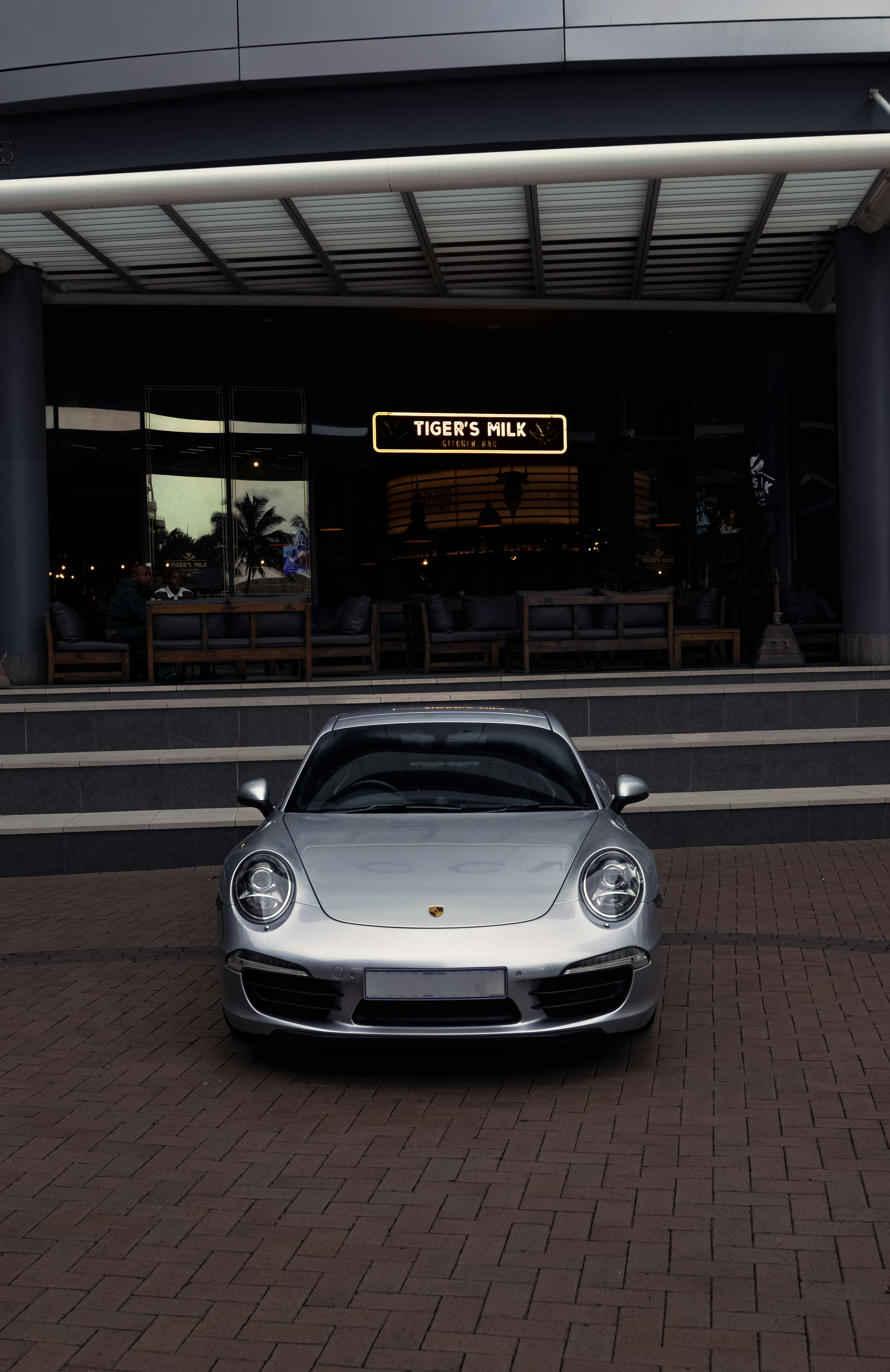 A silver porsche parked in front of a restaurant.