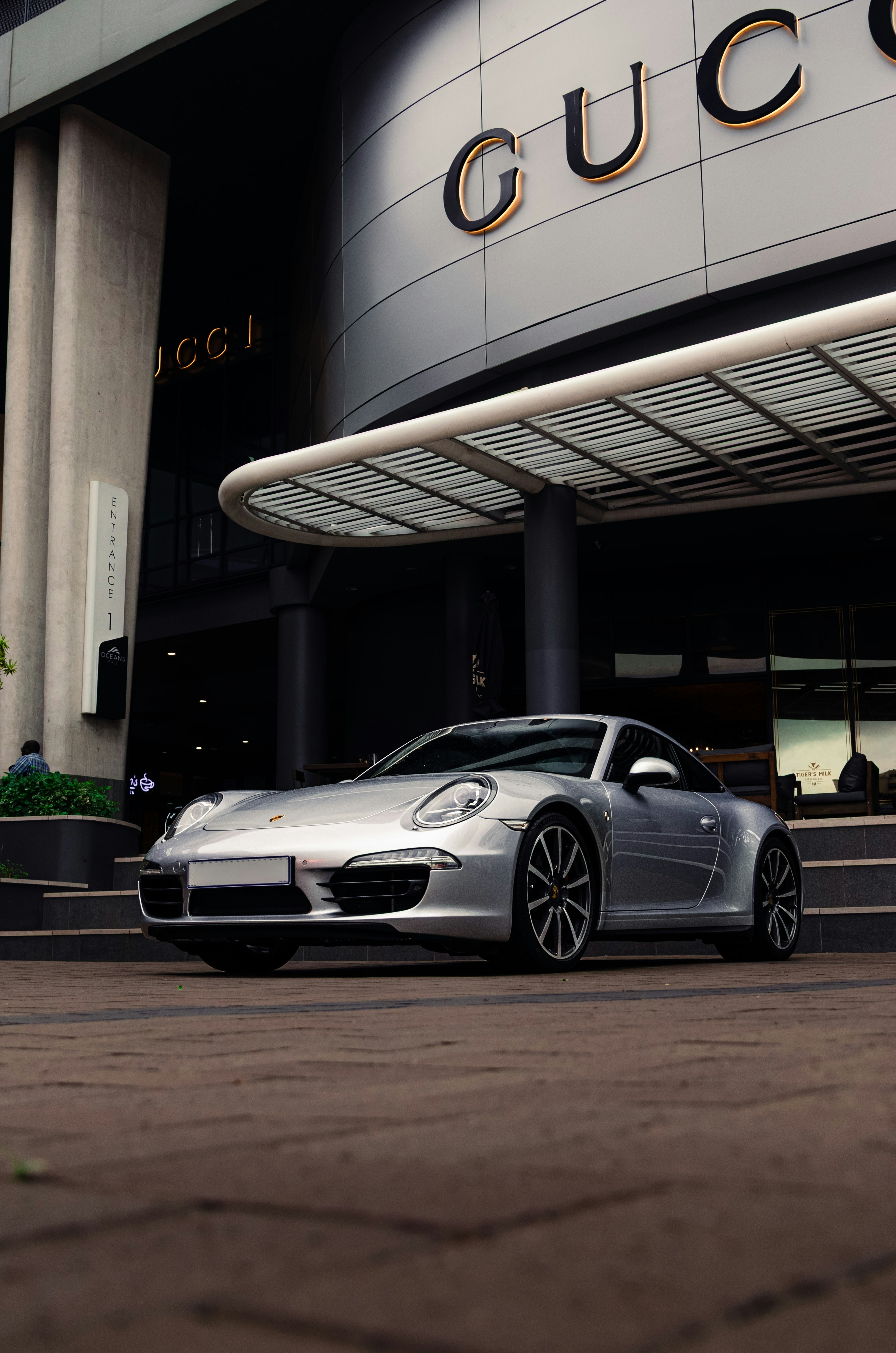 A silver porsche sits in front of a gucci store.