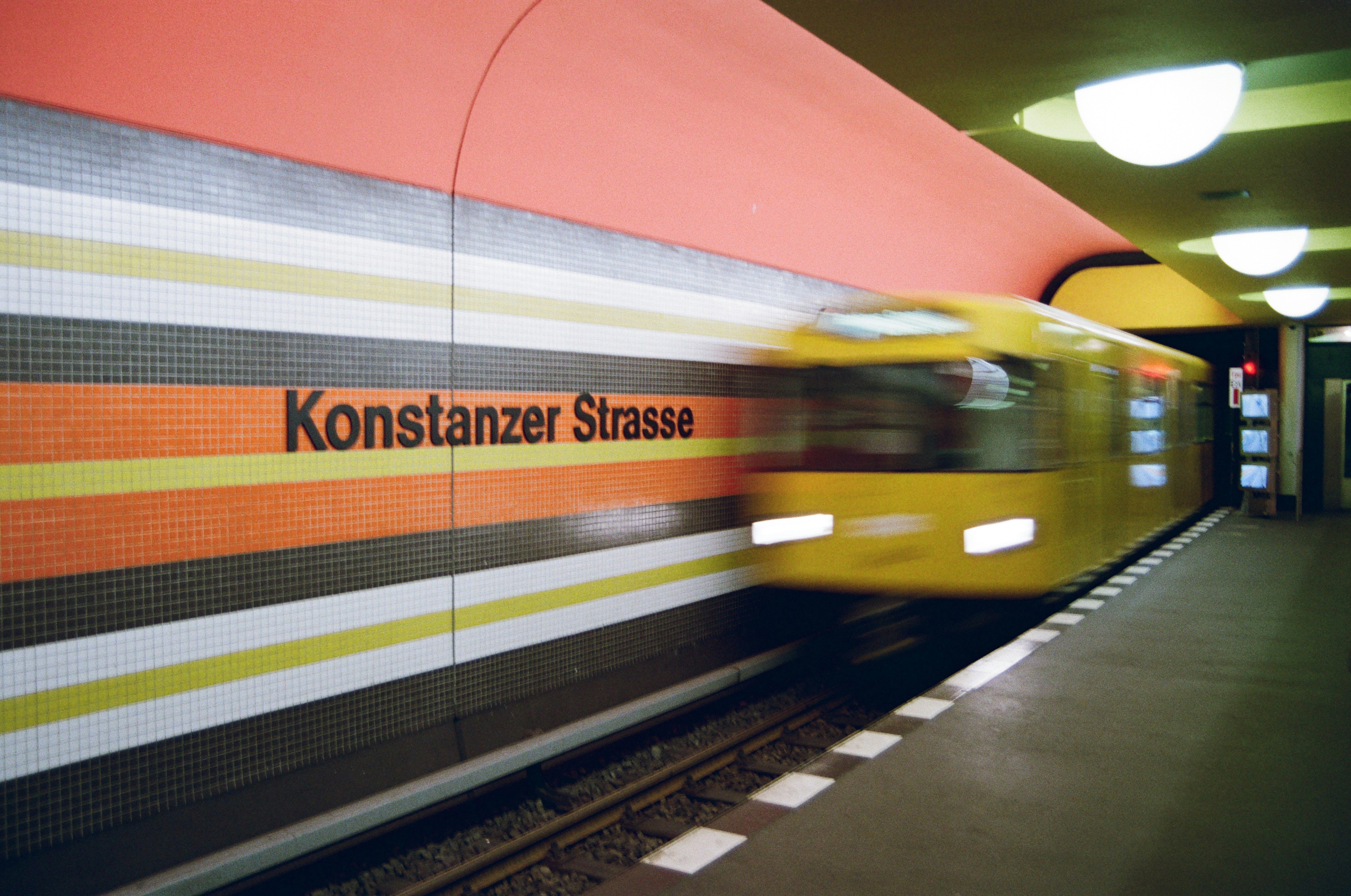A yellow train speeds past the station sign.