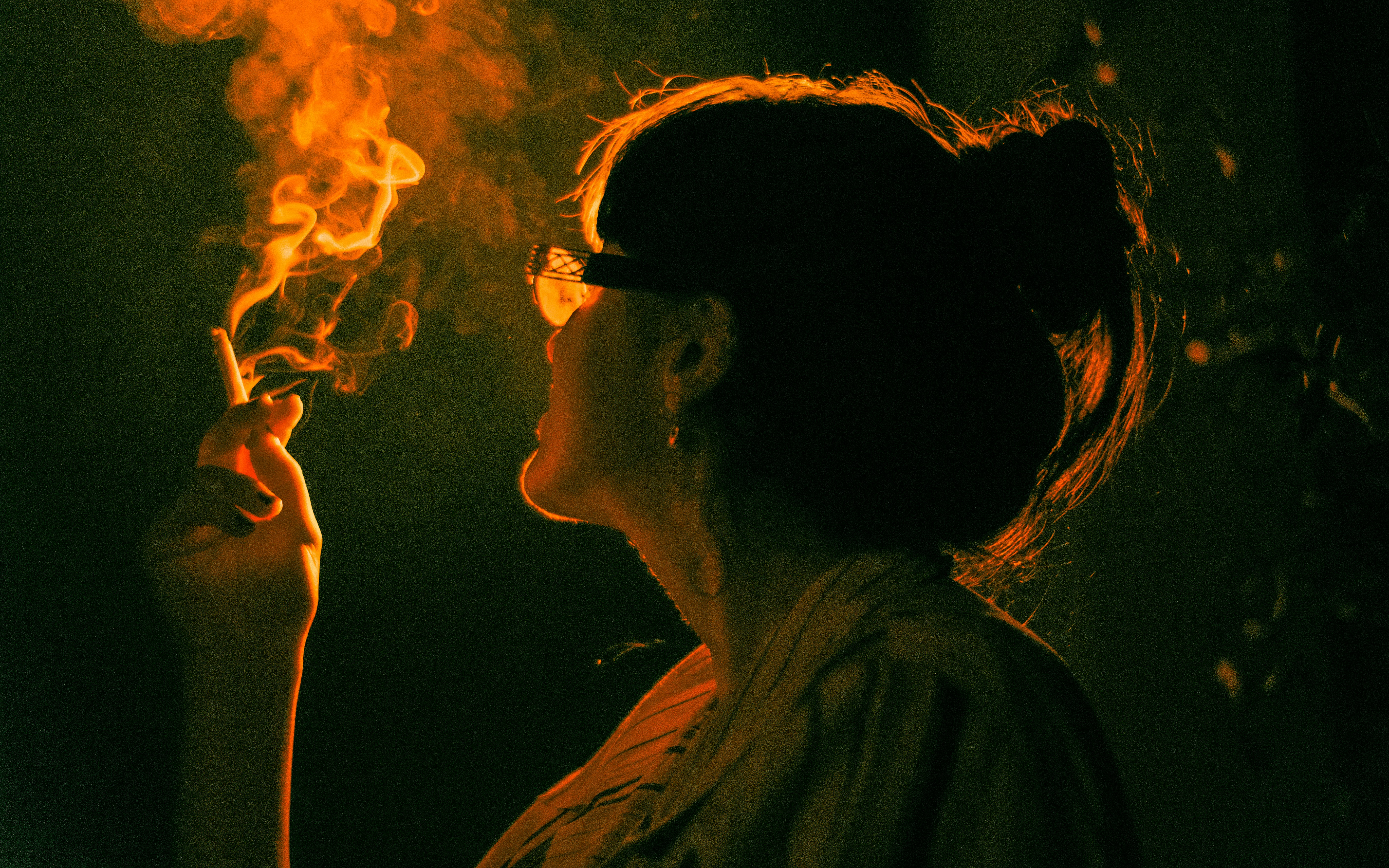 A woman smokes a cigarette, backlit by orange light.
