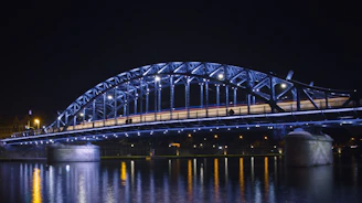 A lit-up bridge shimmers over water at night.