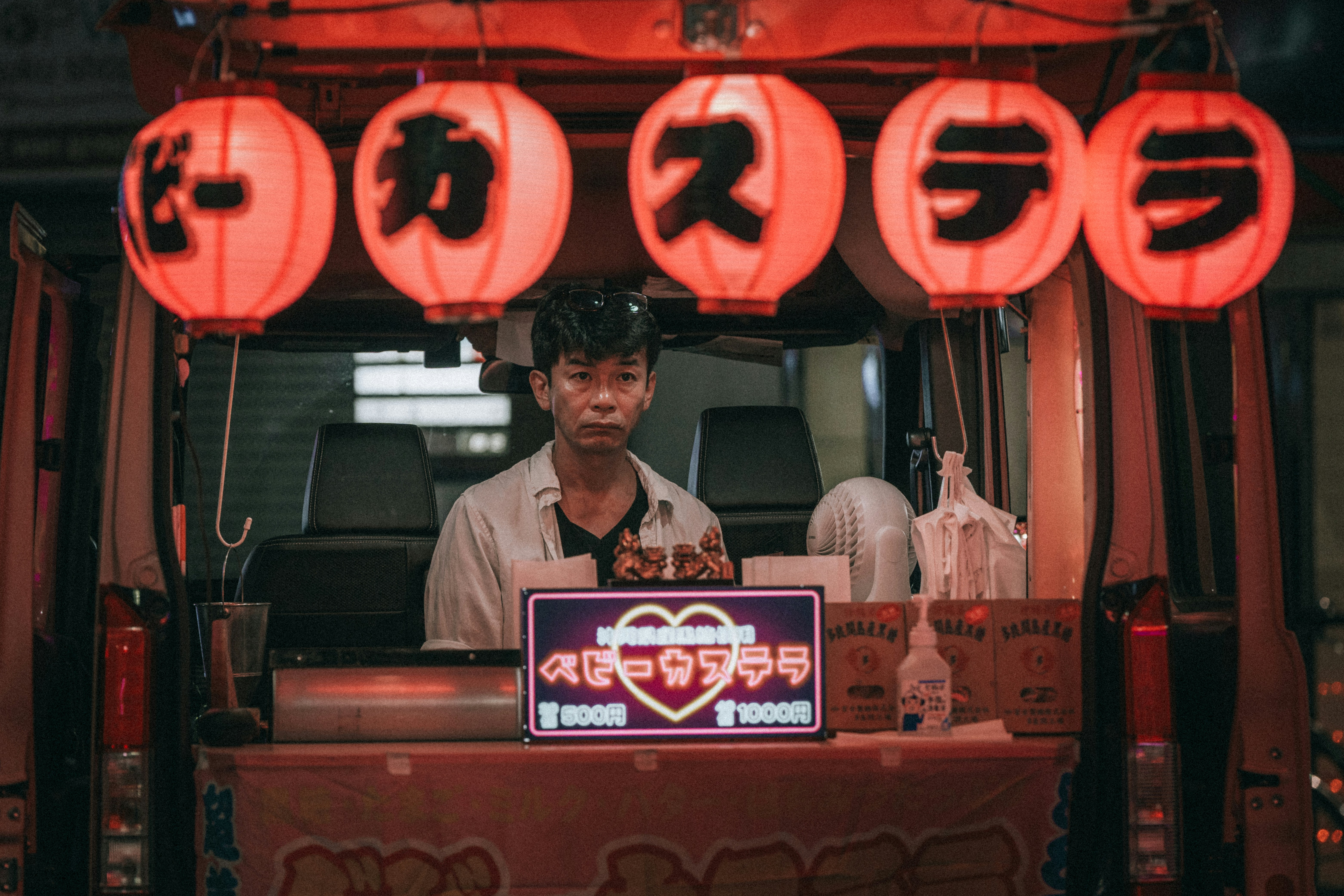 A street vendor stands beneath bright red lanterns.