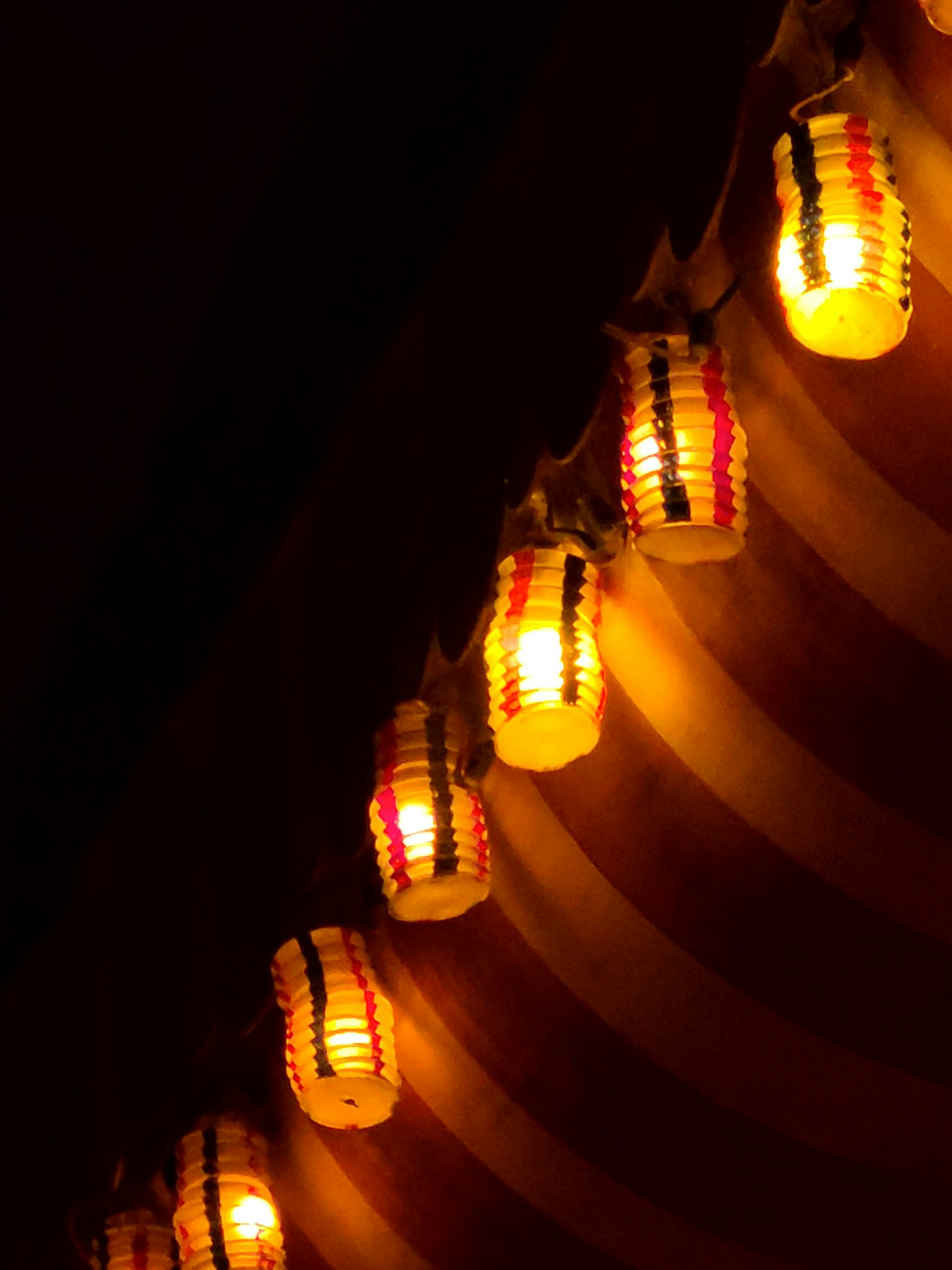 Lit paper lanterns illuminate a striped ceiling.
