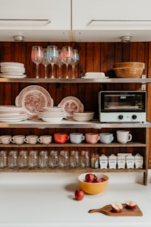 A kitchen shelf displays dishes, glasses, and jars.