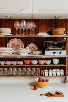 A kitchen shelf displays dishes, glasses, and jars.