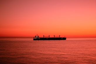 A ship sails on the ocean at sunset.