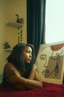 Young woman sits by a painting in a room.