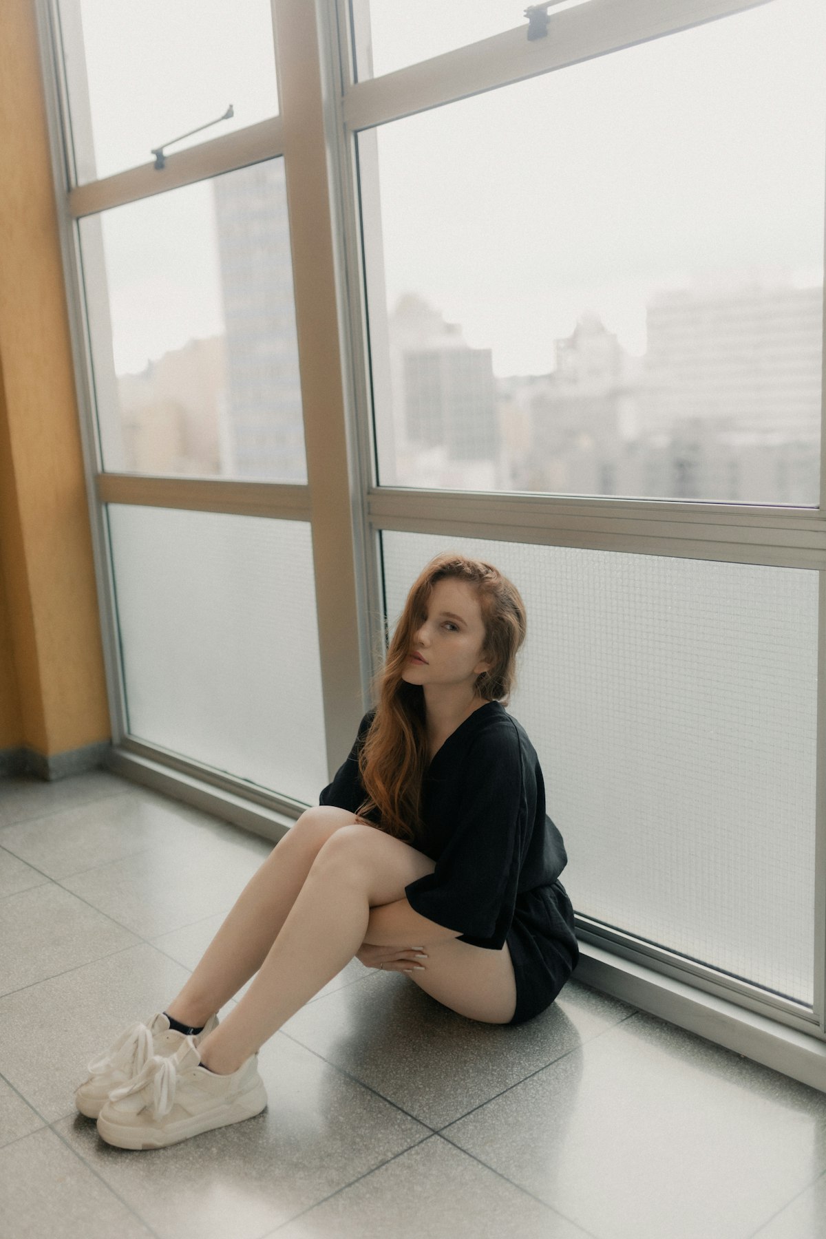 A woman sits by a window, gazing thoughtfully