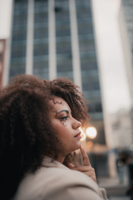 A woman contemplates against a tall, urban backdrop.