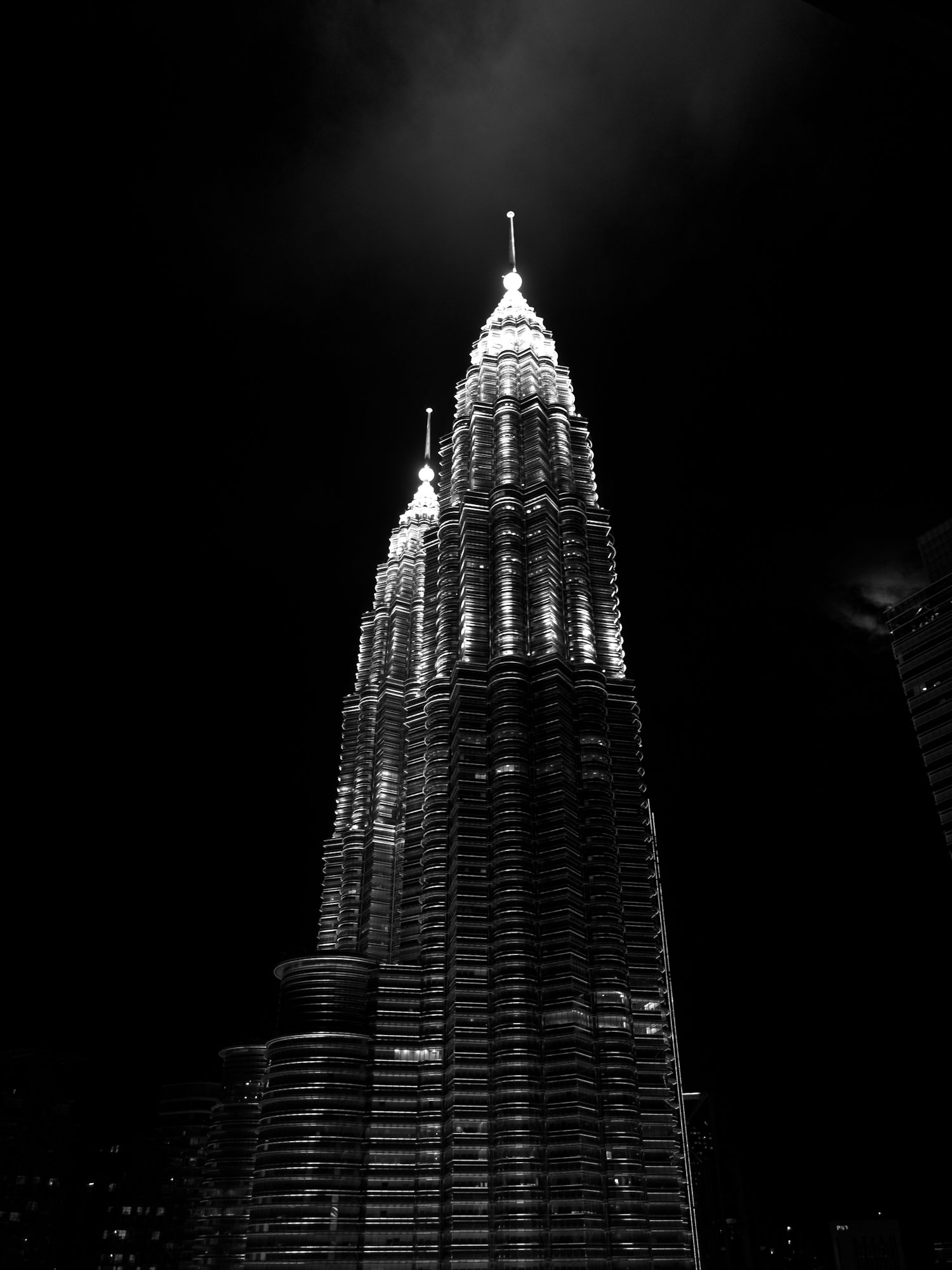 A black and white photo of the Petronas Towers at night, their illuminated facades and spires reaching into the dark sky.