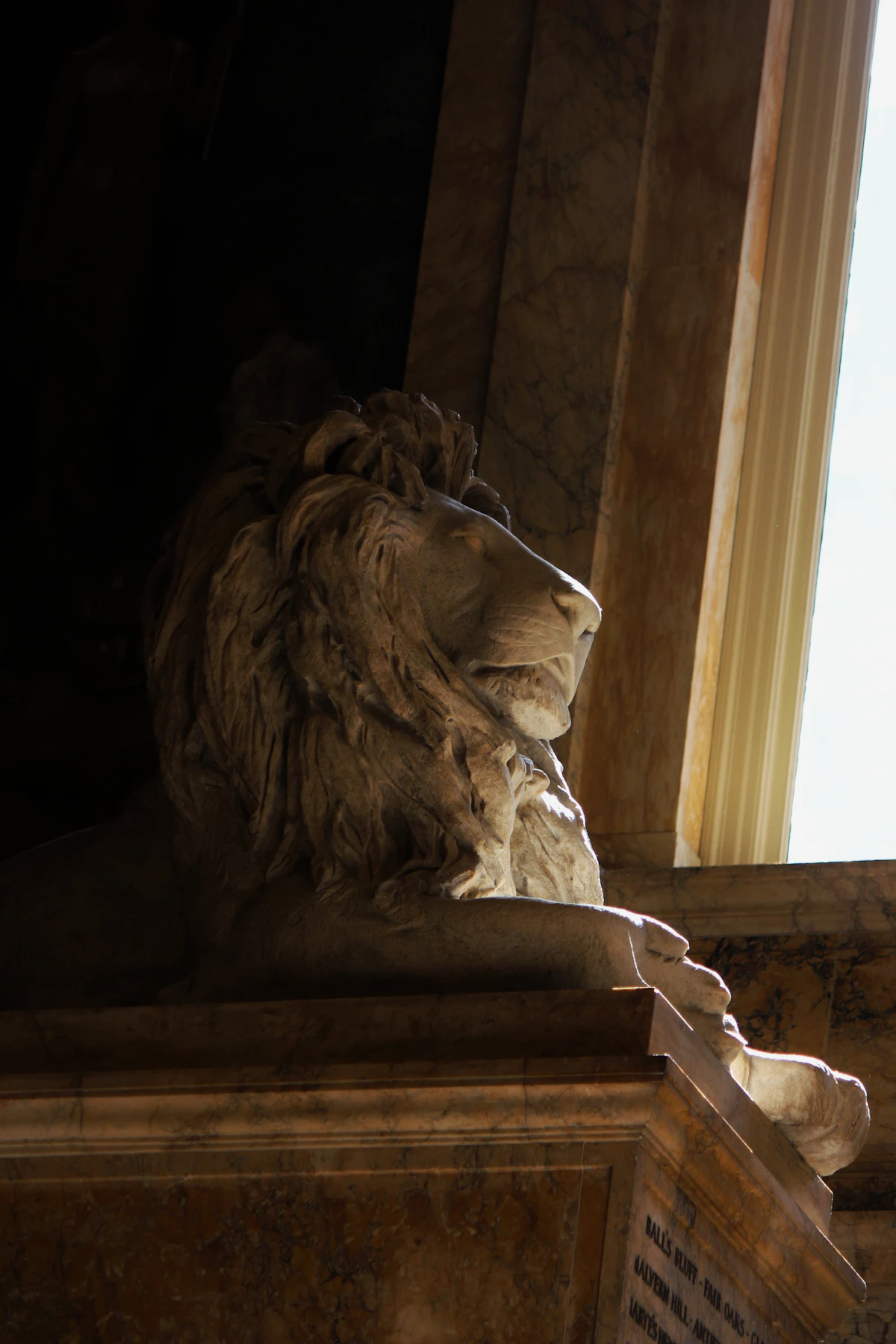 A carved stone lion resting on a marble plinth, lit from a tall window
