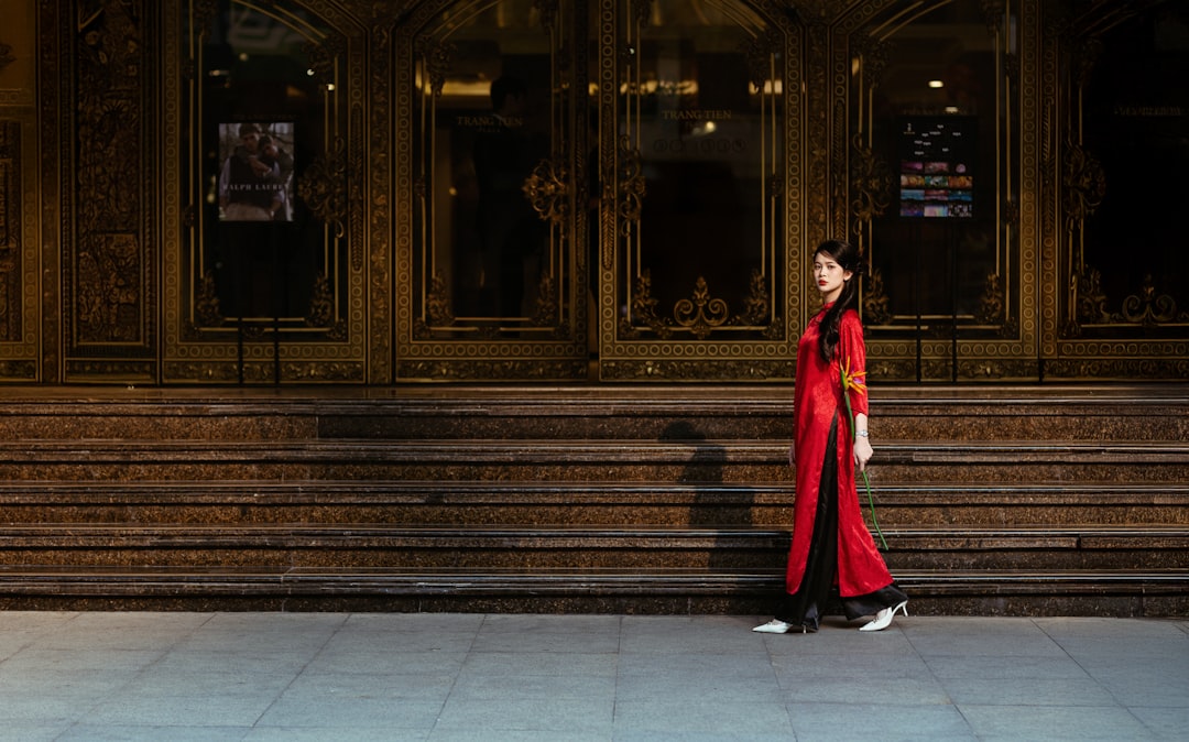 Woman in red dress stands before grand doors.