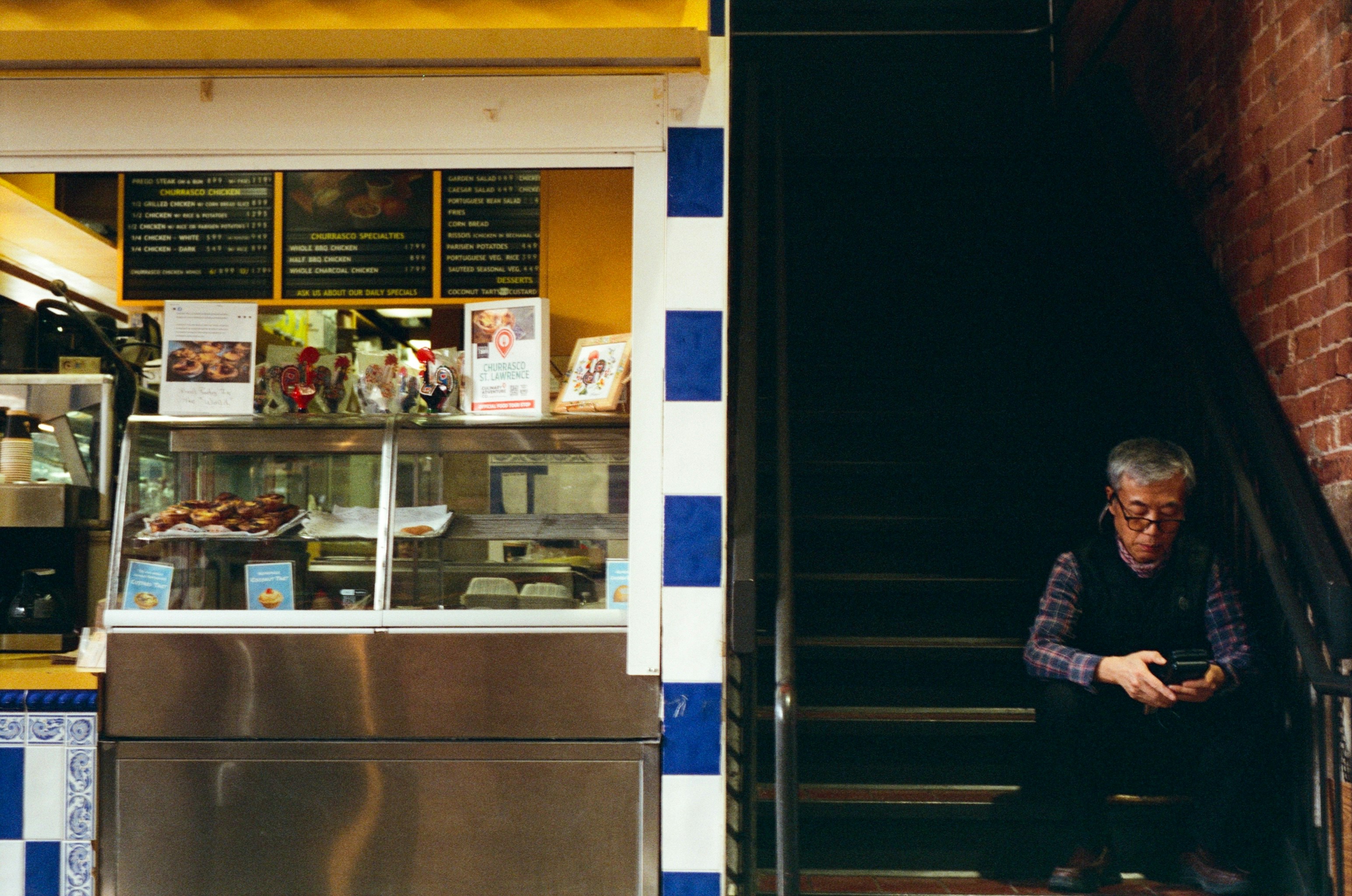 An elderly man sits on stairs beside a cafe.