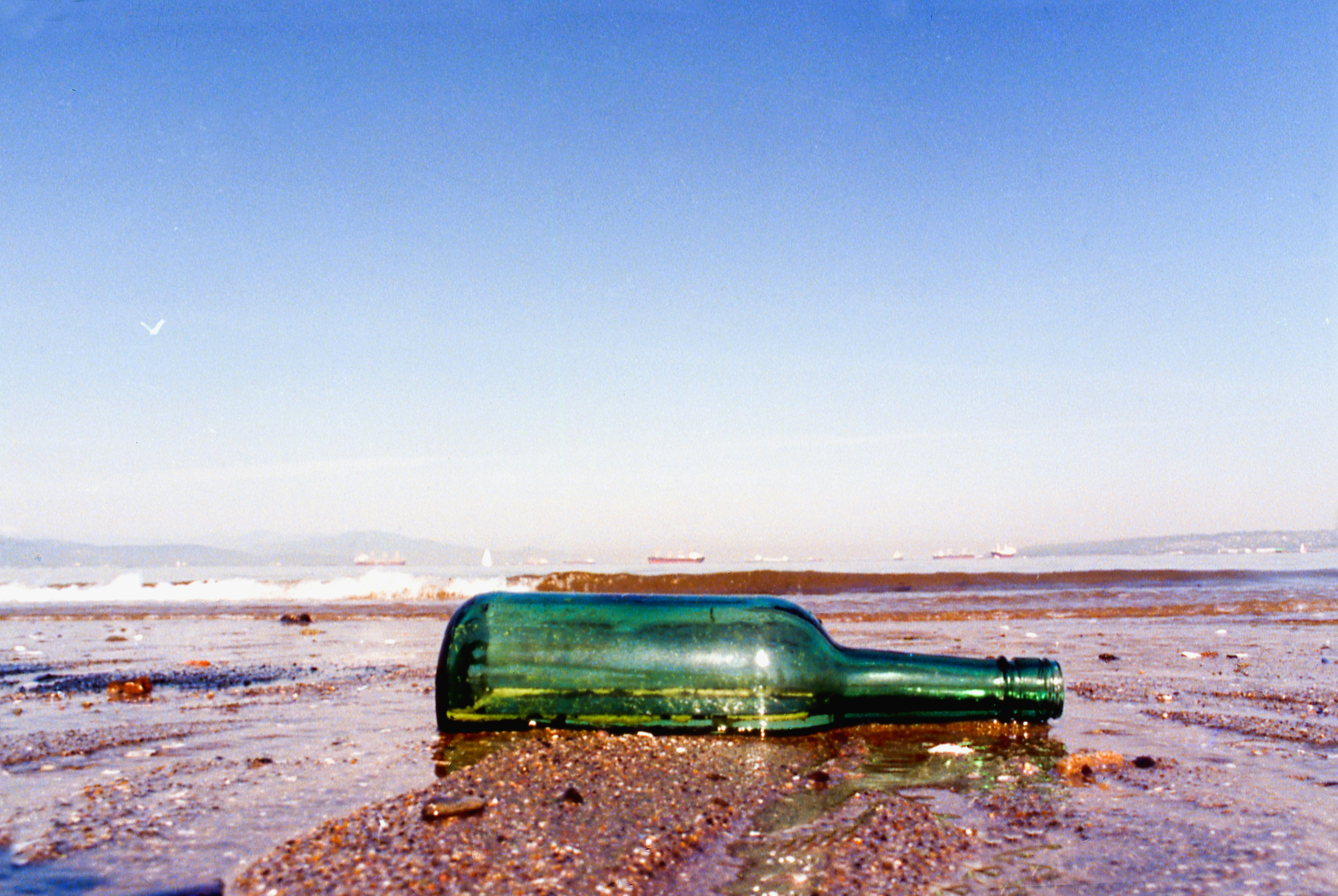 A green bottle lies on a sandy beach.