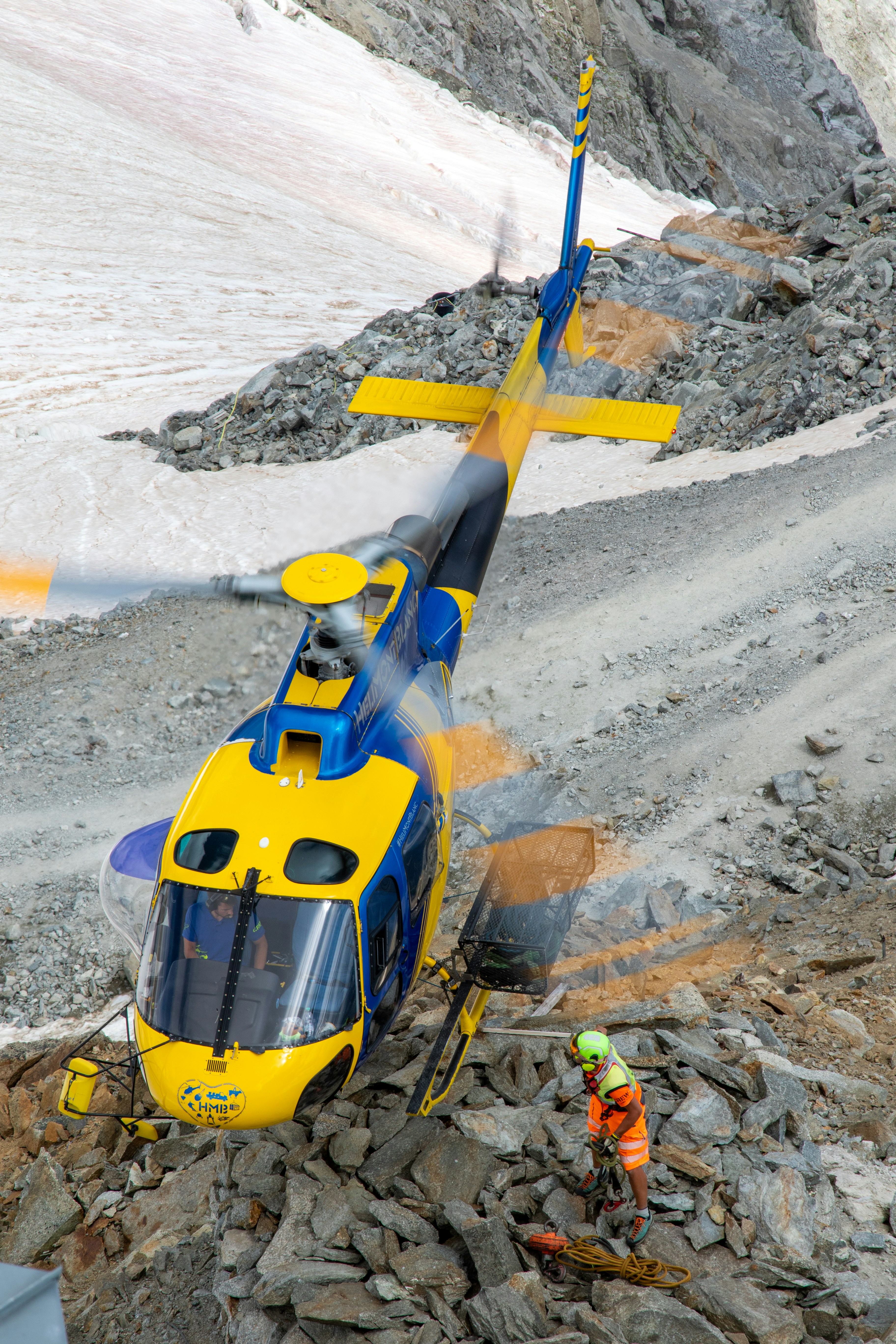 A helicopter lands in a snowy, rocky mountain area.
