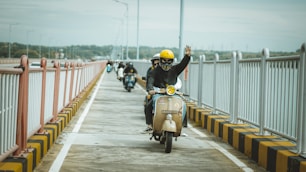 Scooter riders wave while crossing a bridge.