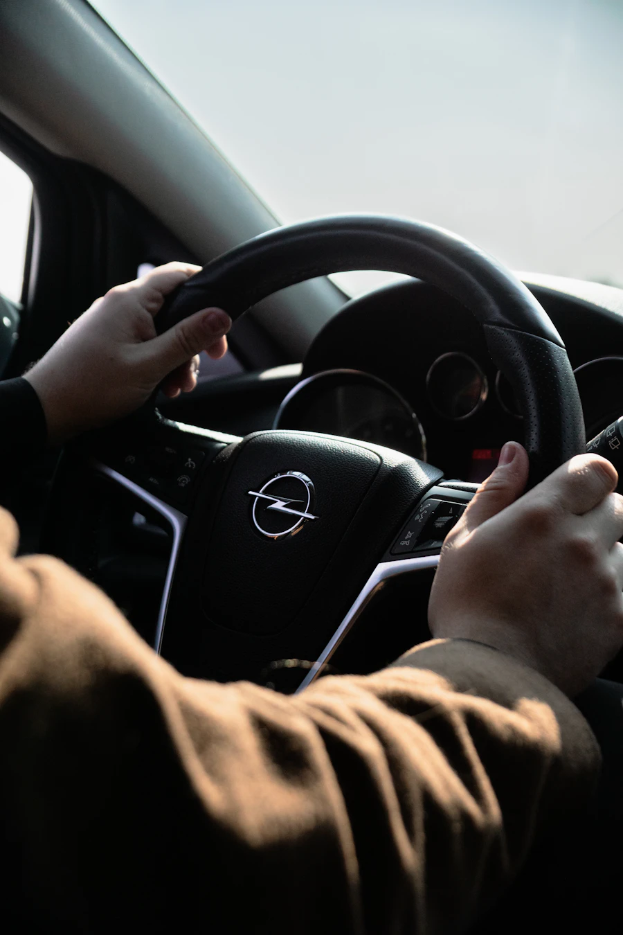 A learner's hands resting on a car steering wheel in soft daylight