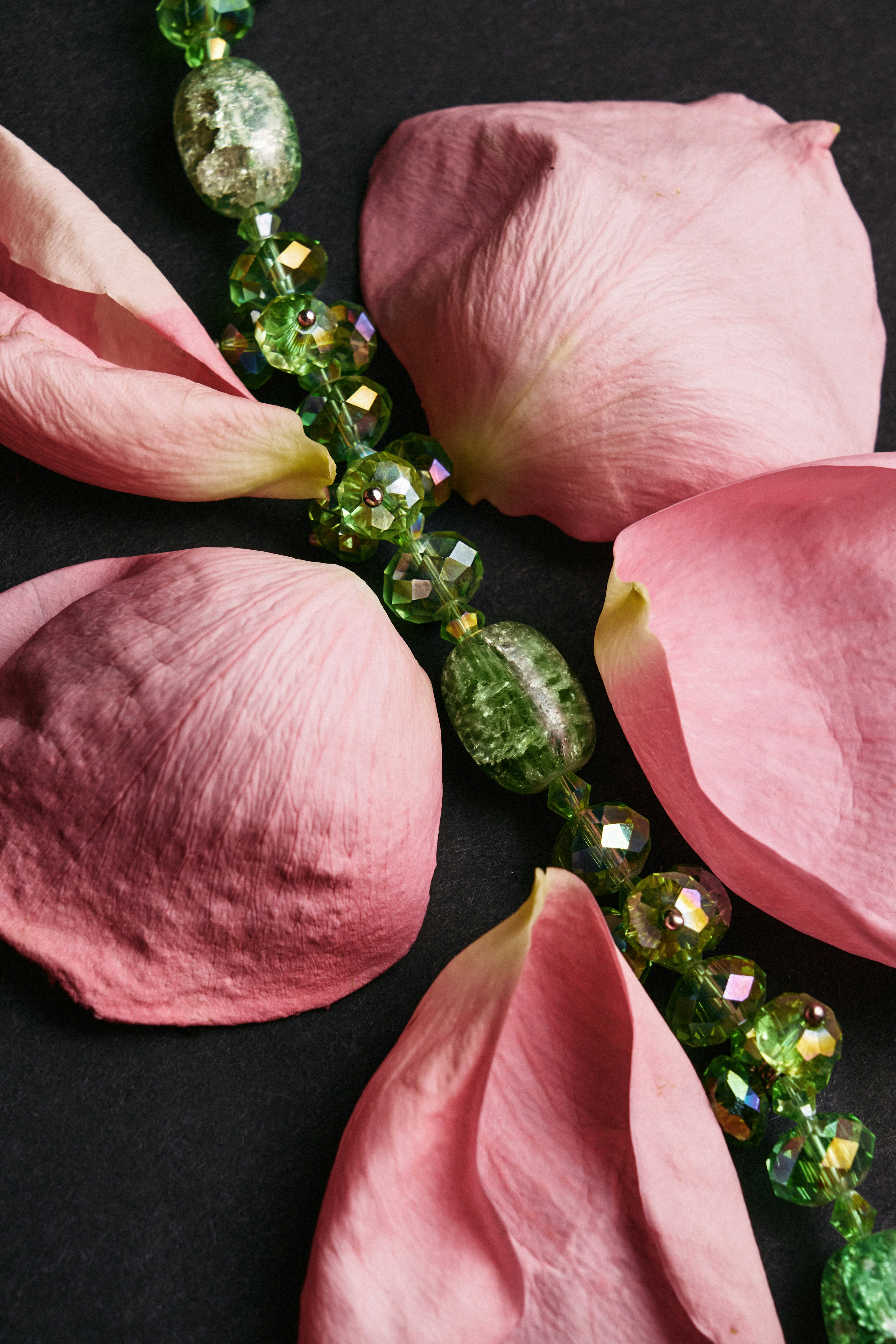 Pink petals surround a sparkling green beaded necklace.