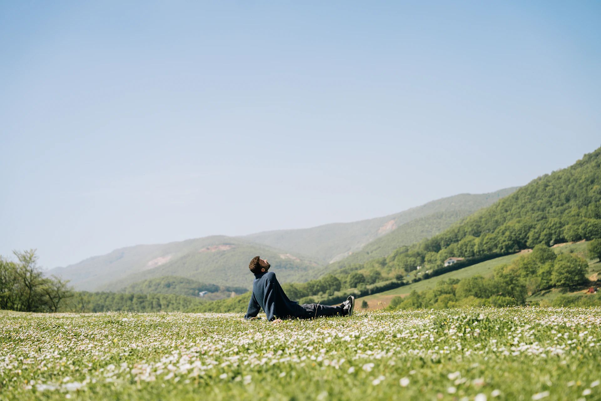 Person does yoga on a grassy field near mountains.