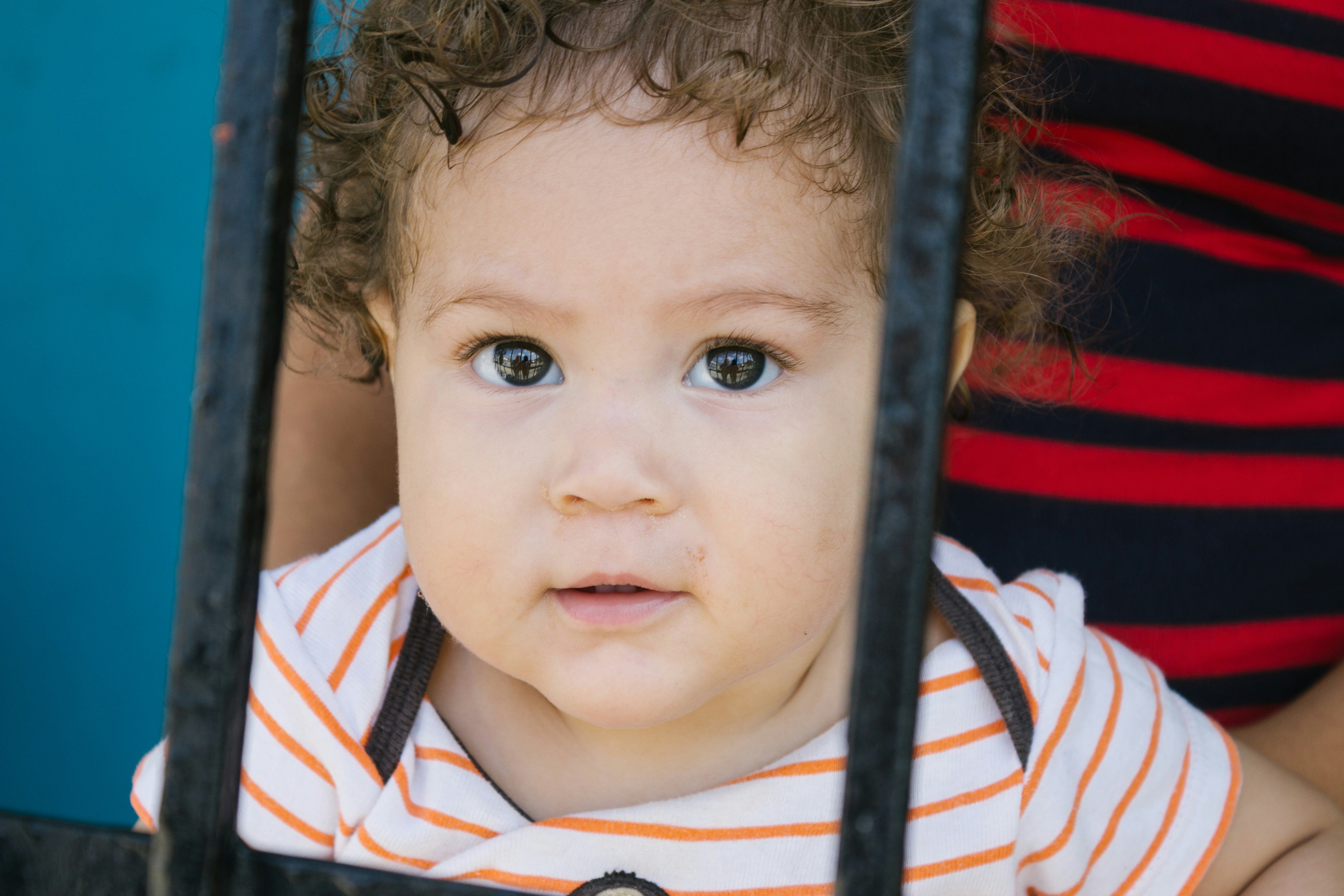A cute baby looks through a barred window.