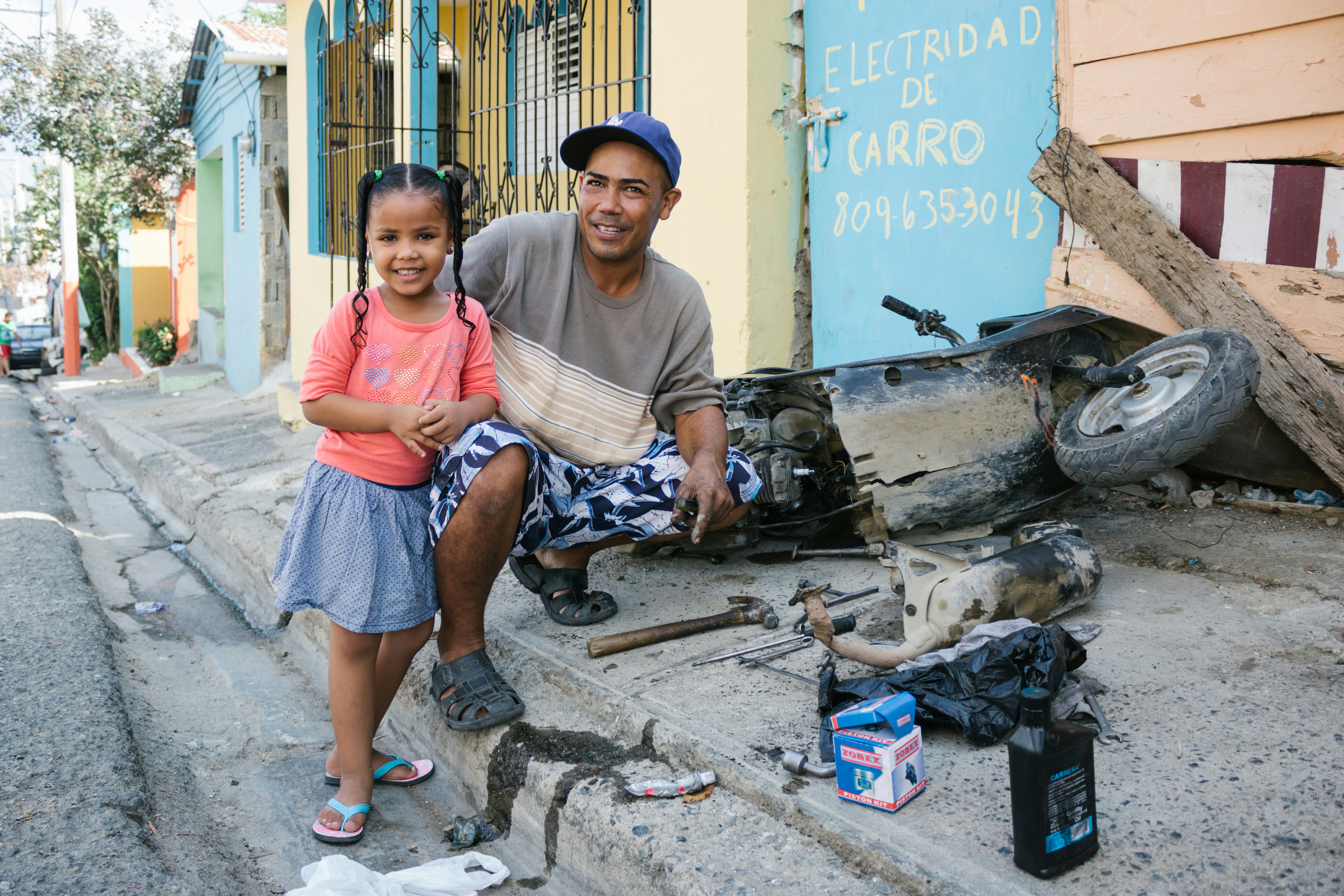 A father and daughter pose near a damaged car.