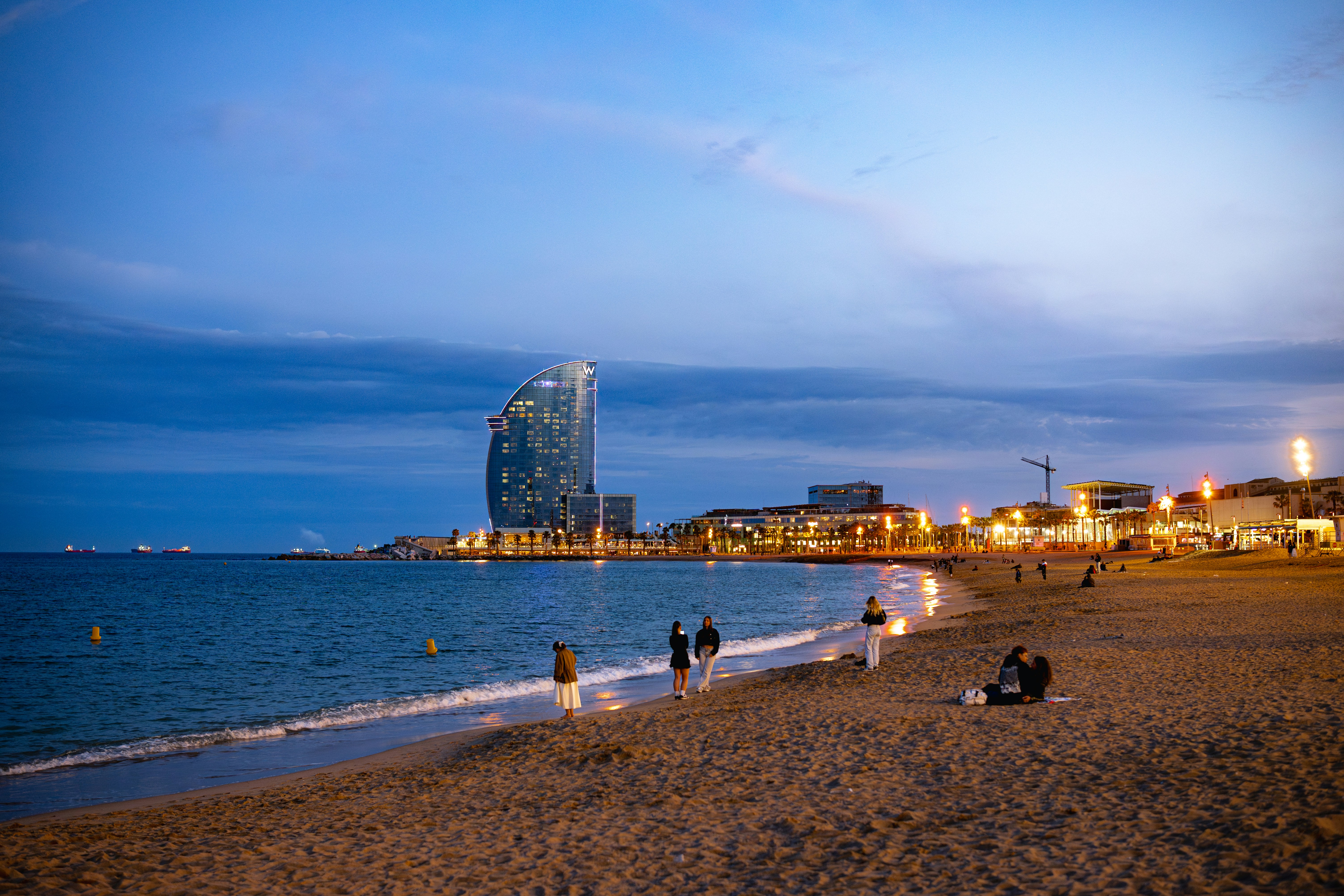 Beachgoers enjoy the view of barcelona at twilight.