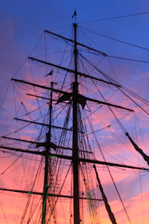 Tall ship's masts silhouetted against a sunset sky.