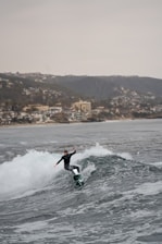 A surfer rides a wave near the coast.