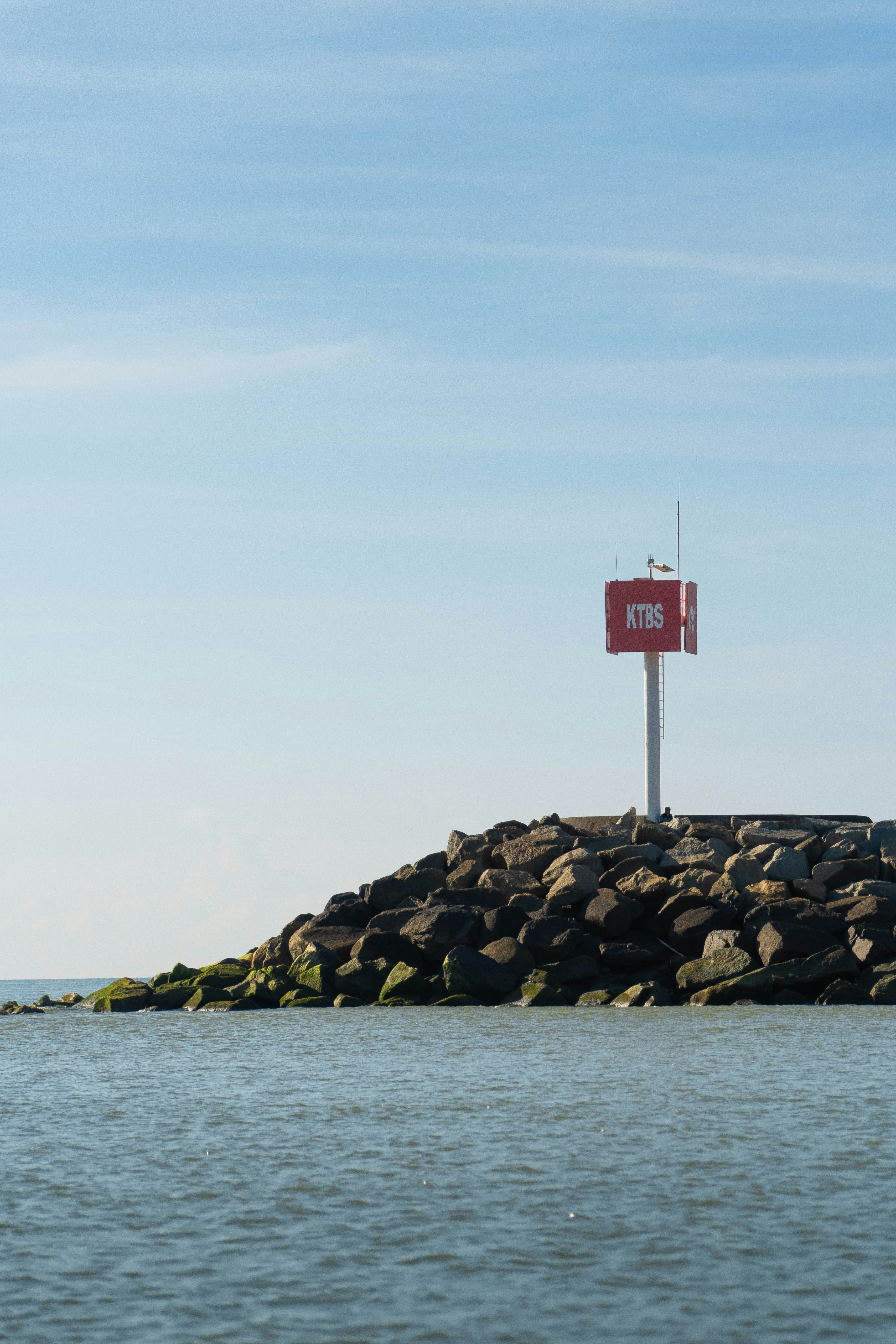 A red navigation marker stands on a rocky breakwater