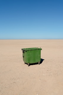 A green dumpster sits alone in the desert.