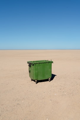 A green dumpster sits alone in the desert.